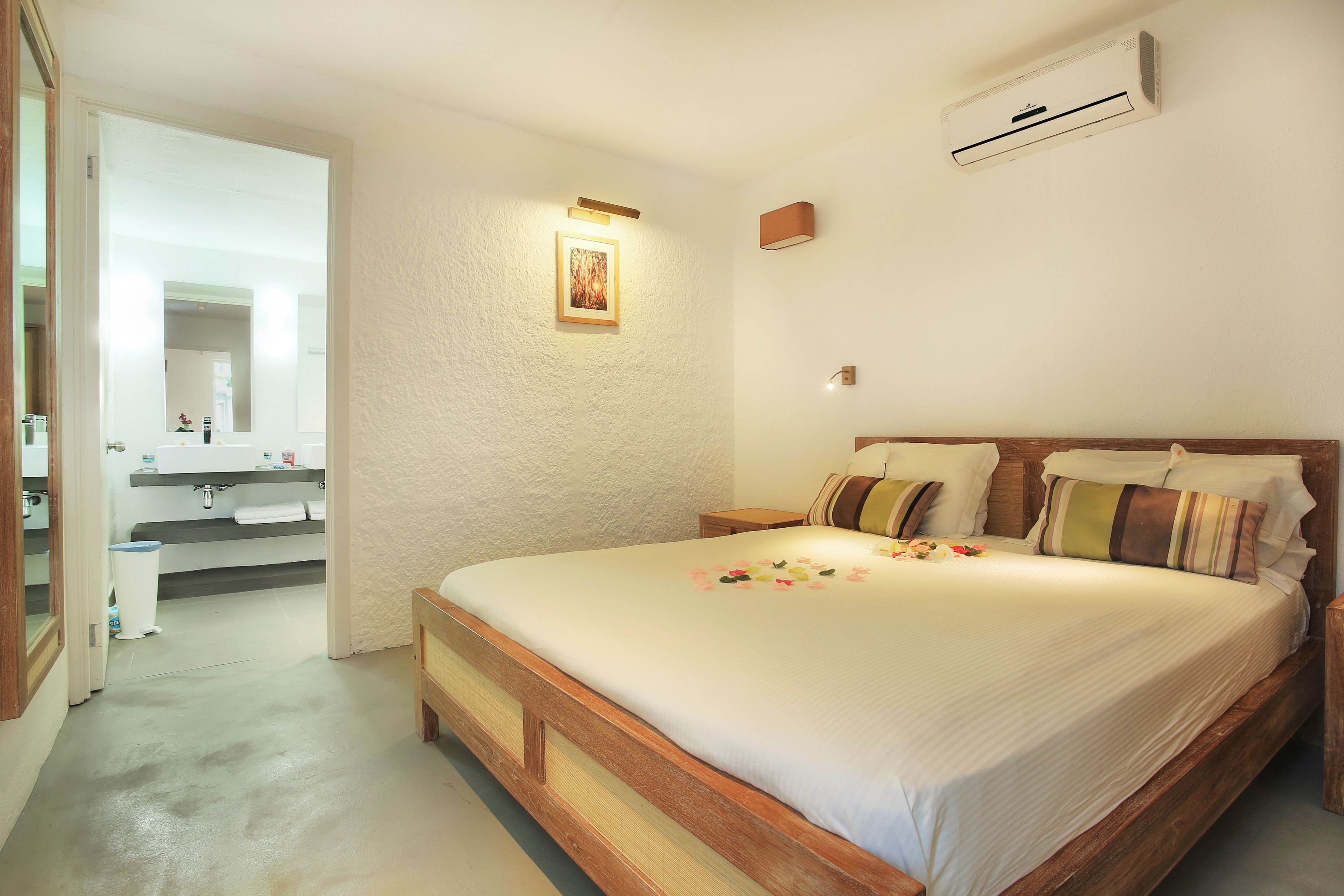 A bedroom with a wooden bed, a nightstand, a wall-mounted air conditioner, and a bathroom visible through an open door.