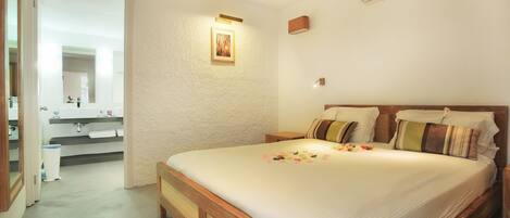 A bedroom with a wooden bed, a nightstand, a wall-mounted air conditioner, and a bathroom visible through an open door.