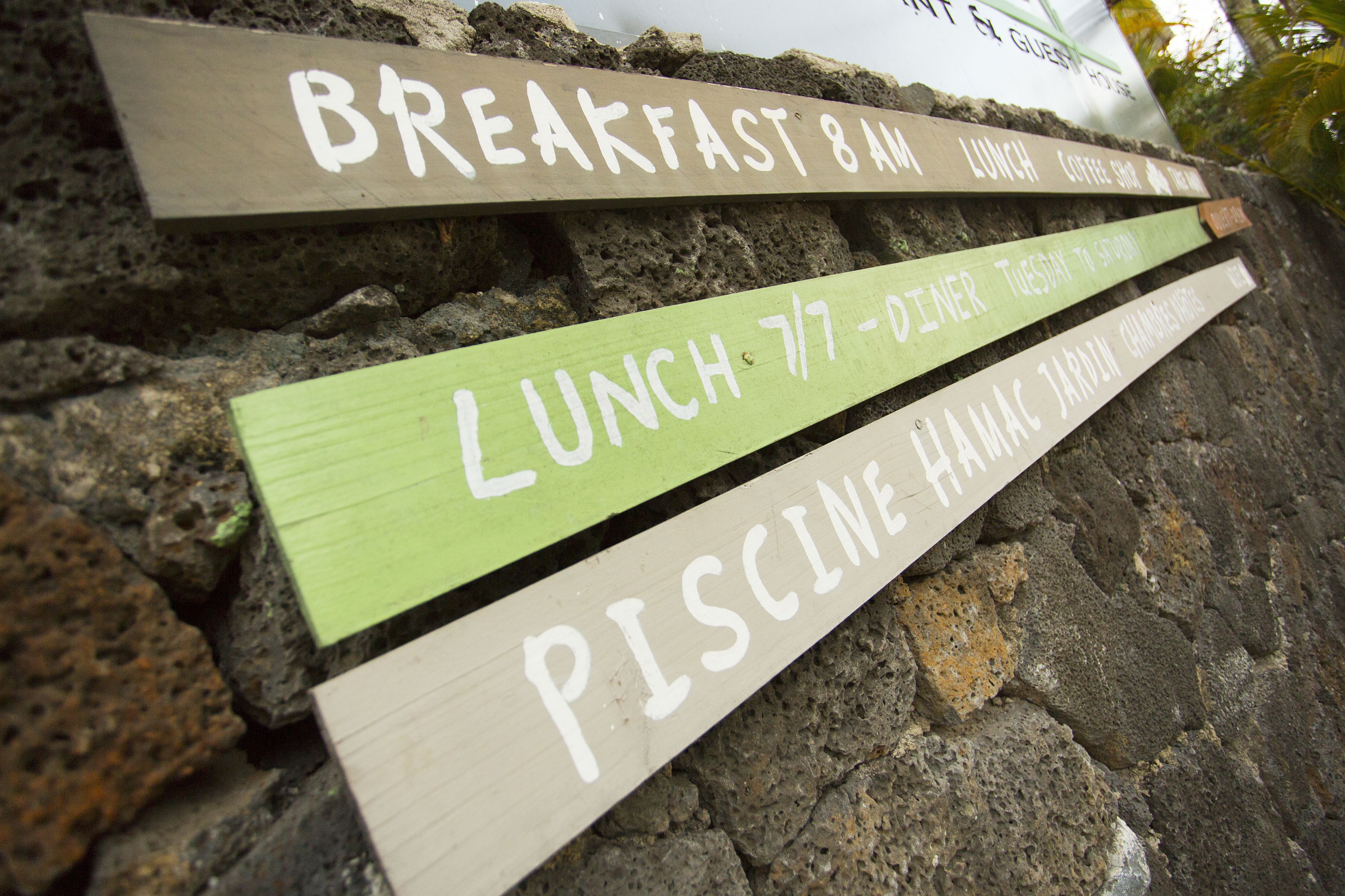 A stone wall with signs indicating breakfast at 8 AM, lunch at 7 PM, and a pool area.