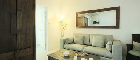 A living room with a sofa, a coffee table with cups and a bowl, a wardrobe, and a mirror on the wall.