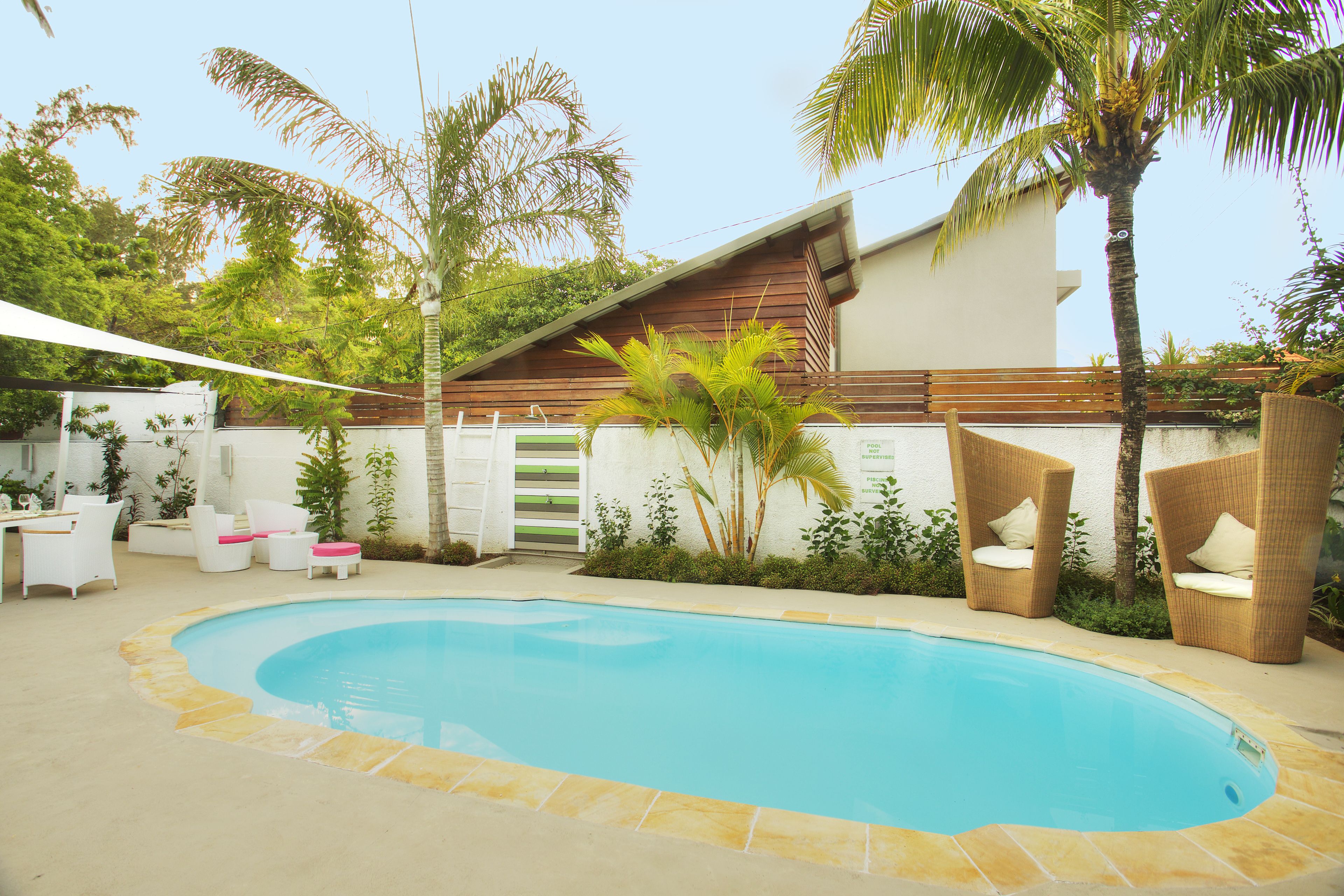 Una piscina con borde de piedra, rodeada de sillas blancas y una valla de madera.