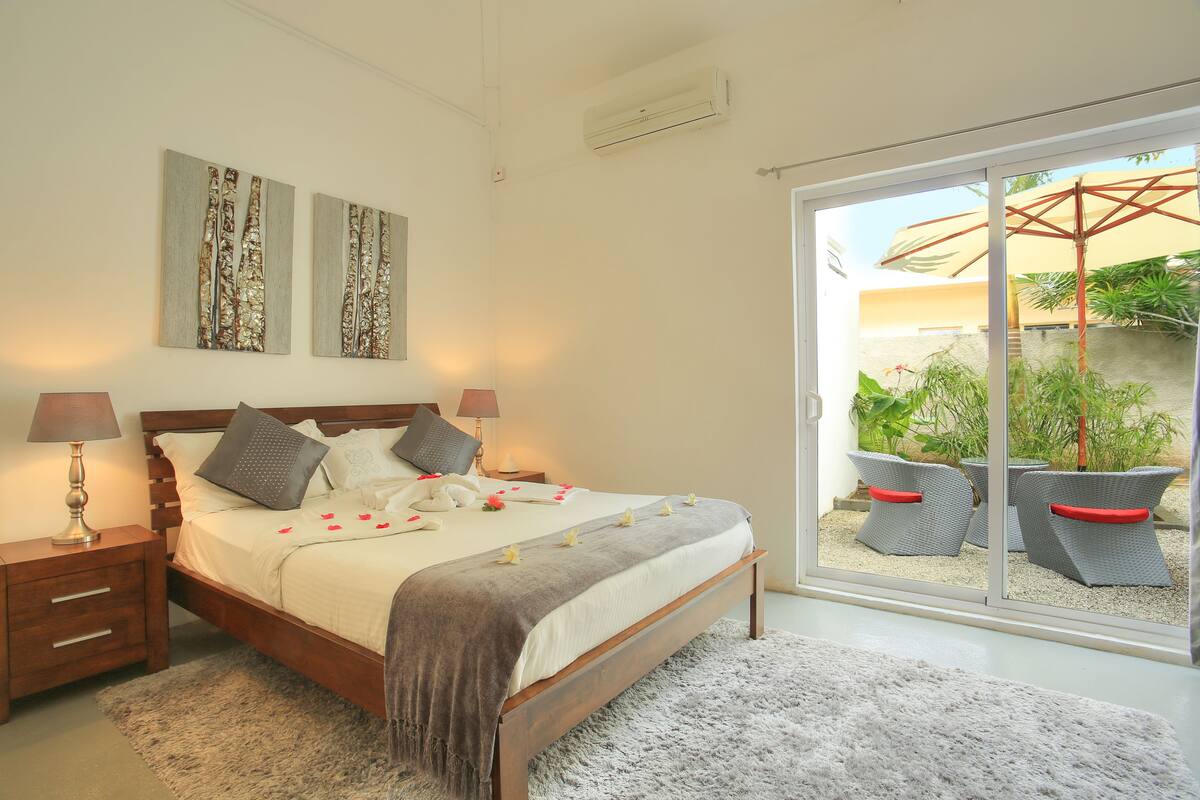 A bedroom with a bed, bedside tables, and a view of an outdoor area with chairs and plants.