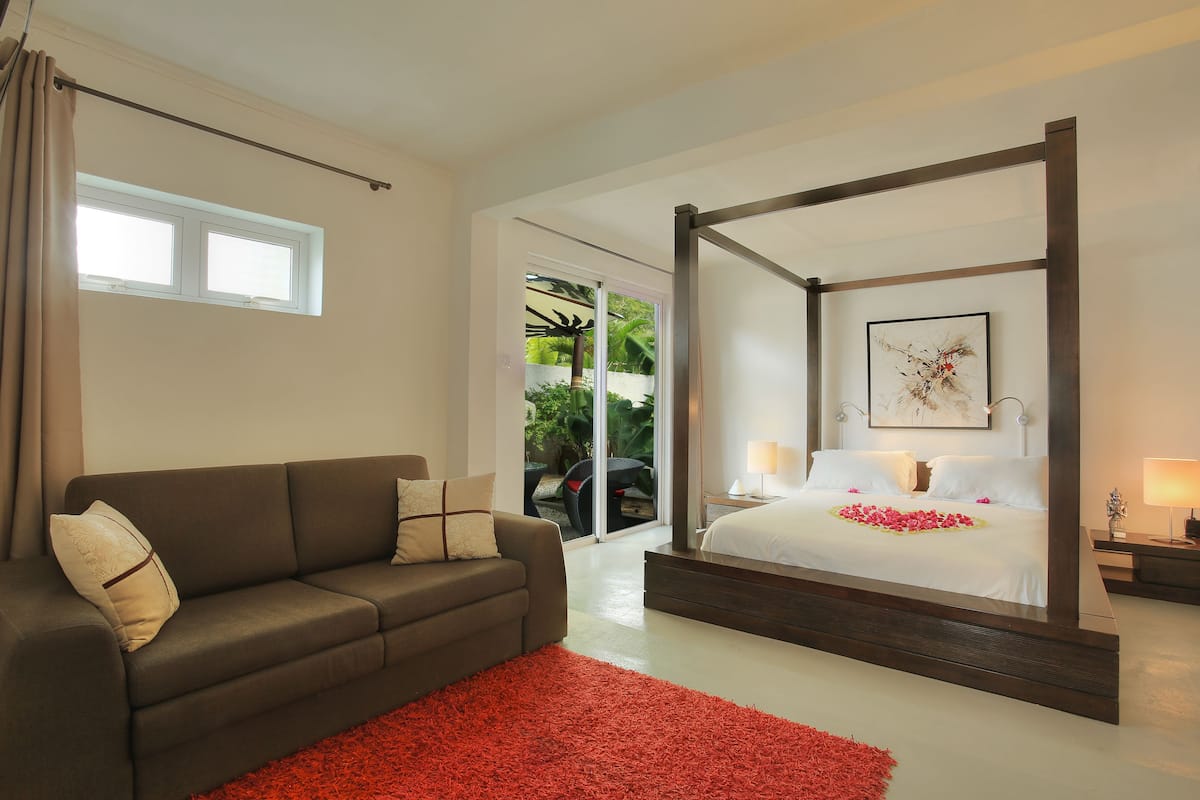 A modern bedroom with a four-poster bed, a sofa, and a red rug.
