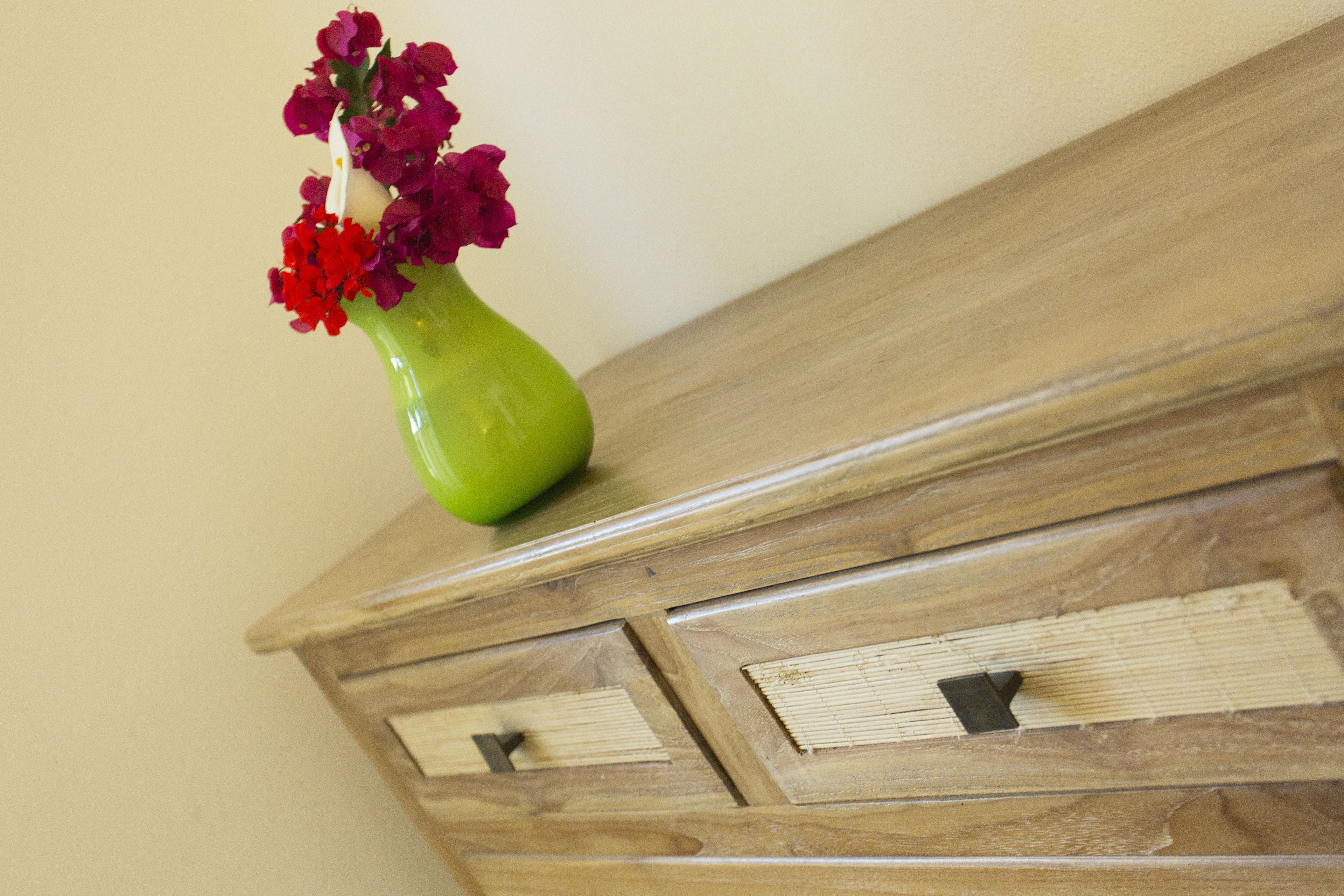 A wooden dresser with two drawers and a green vase with red flowers on top.
