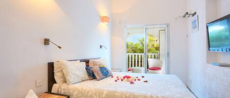 A bedroom with a bed, bedside table, wall-mounted TV, and a balcony with a chair.