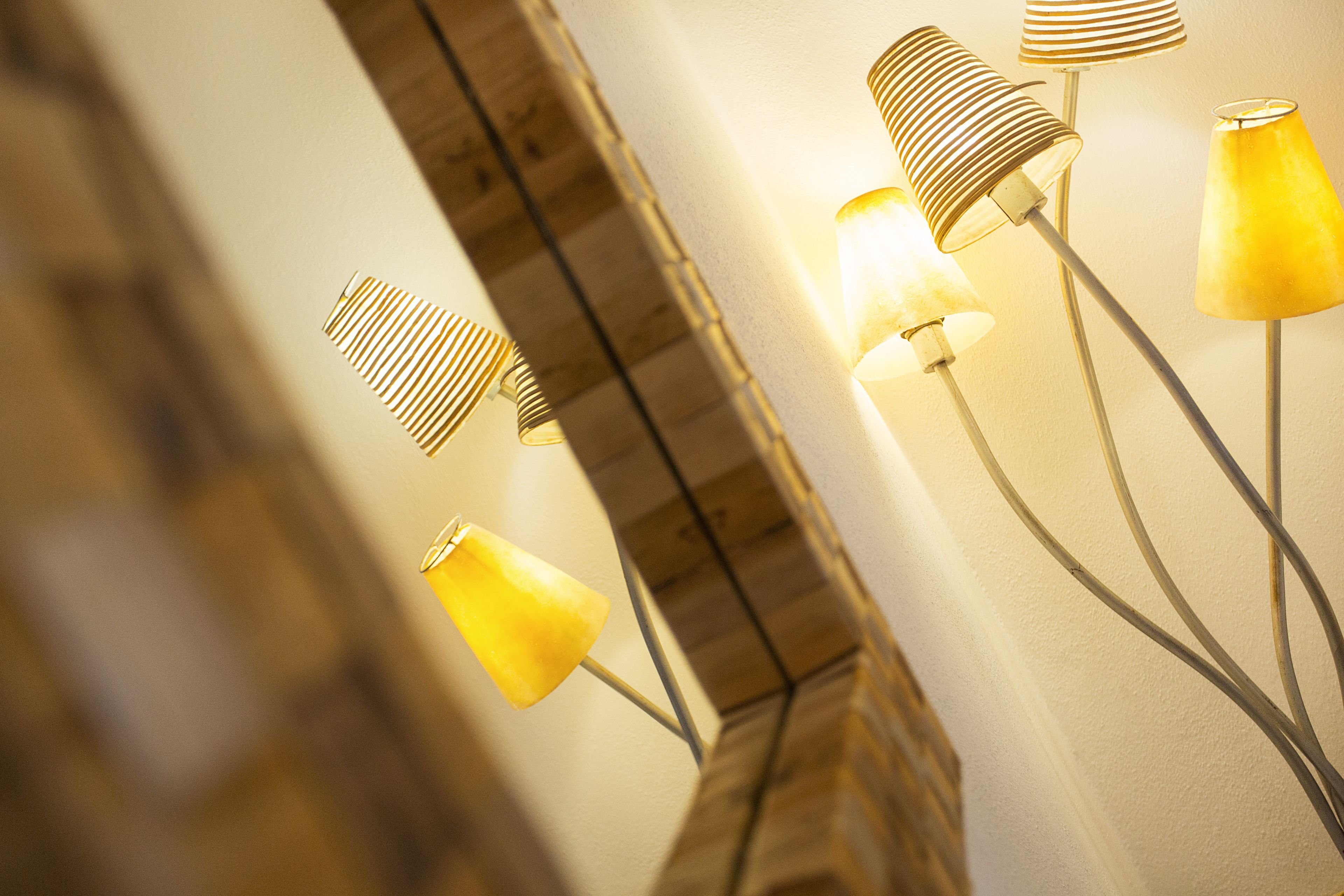 A wall with a mirror and three floor lamps with different shades of yellow.