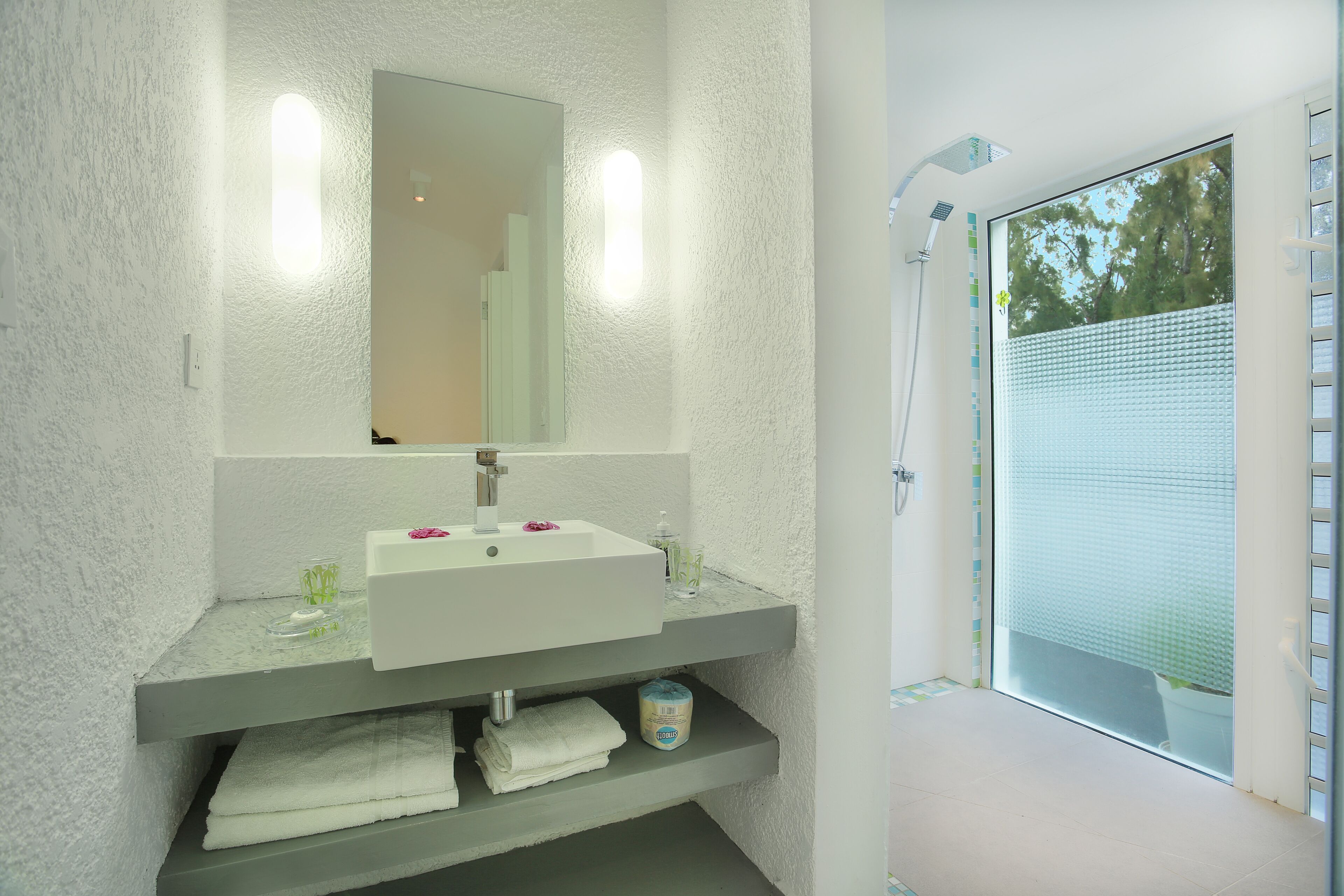A bathroom with a white sink, mirror, and shower. There are towels and a soap dispenser on the sink.