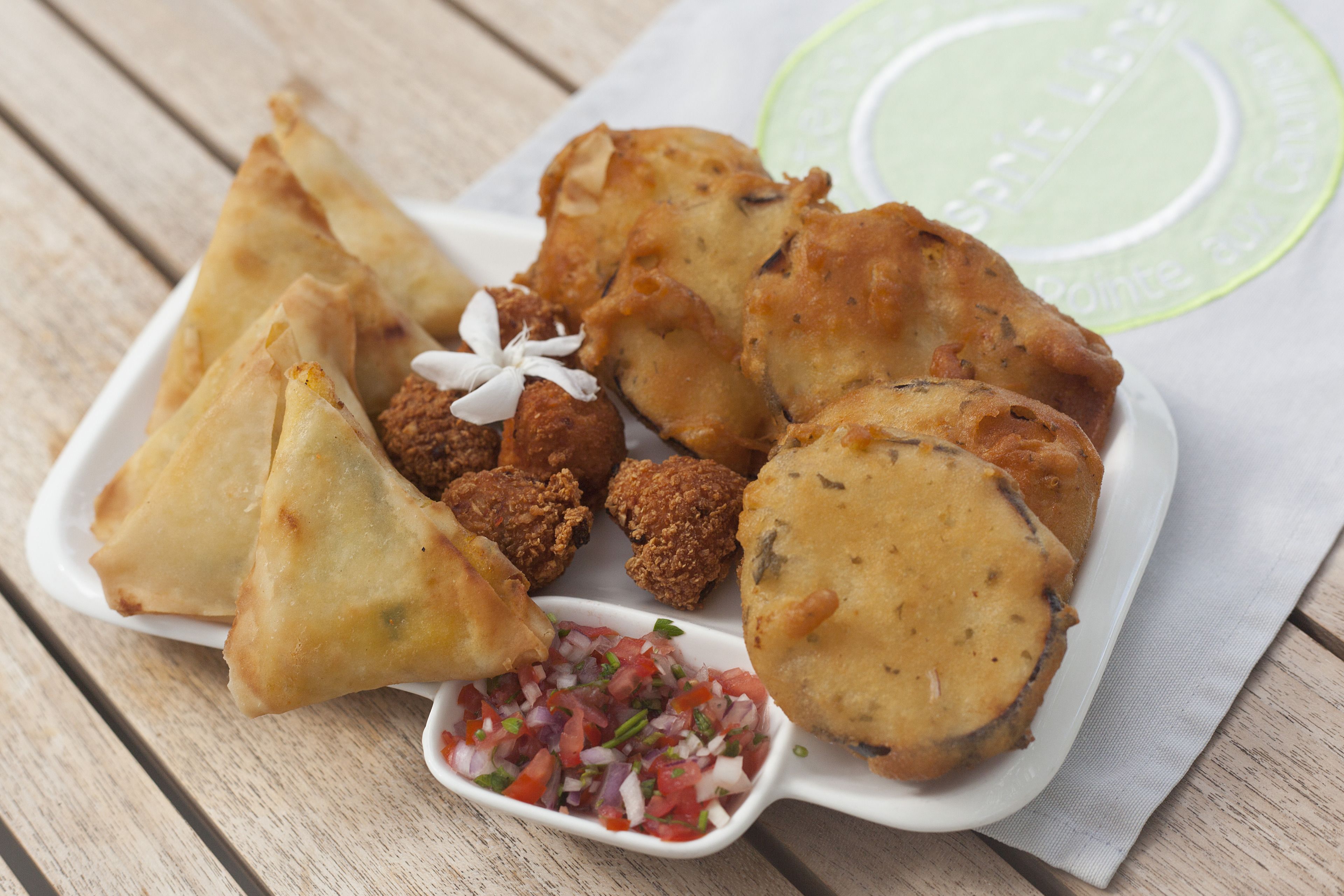 En tallrik med samosas och andra friterade snacks, serverad med hackad lök och koriander.