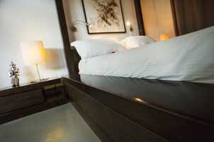 A neatly made bed with white linens, a bedside table with a lamp, and a wall-mounted artwork.