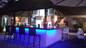 A bar area with stools and a counter, surrounded by a thatched roof structure.