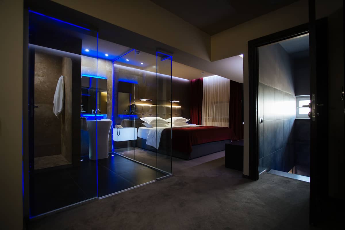 A modern bedroom with a glass-enclosed shower, a bed with white linens, and a red accent wall.