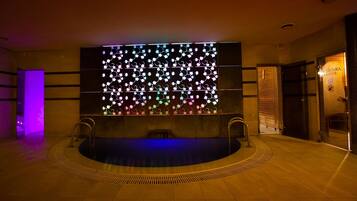 A modern indoor pool area with a central water feature and a decorative light panel on the wall.