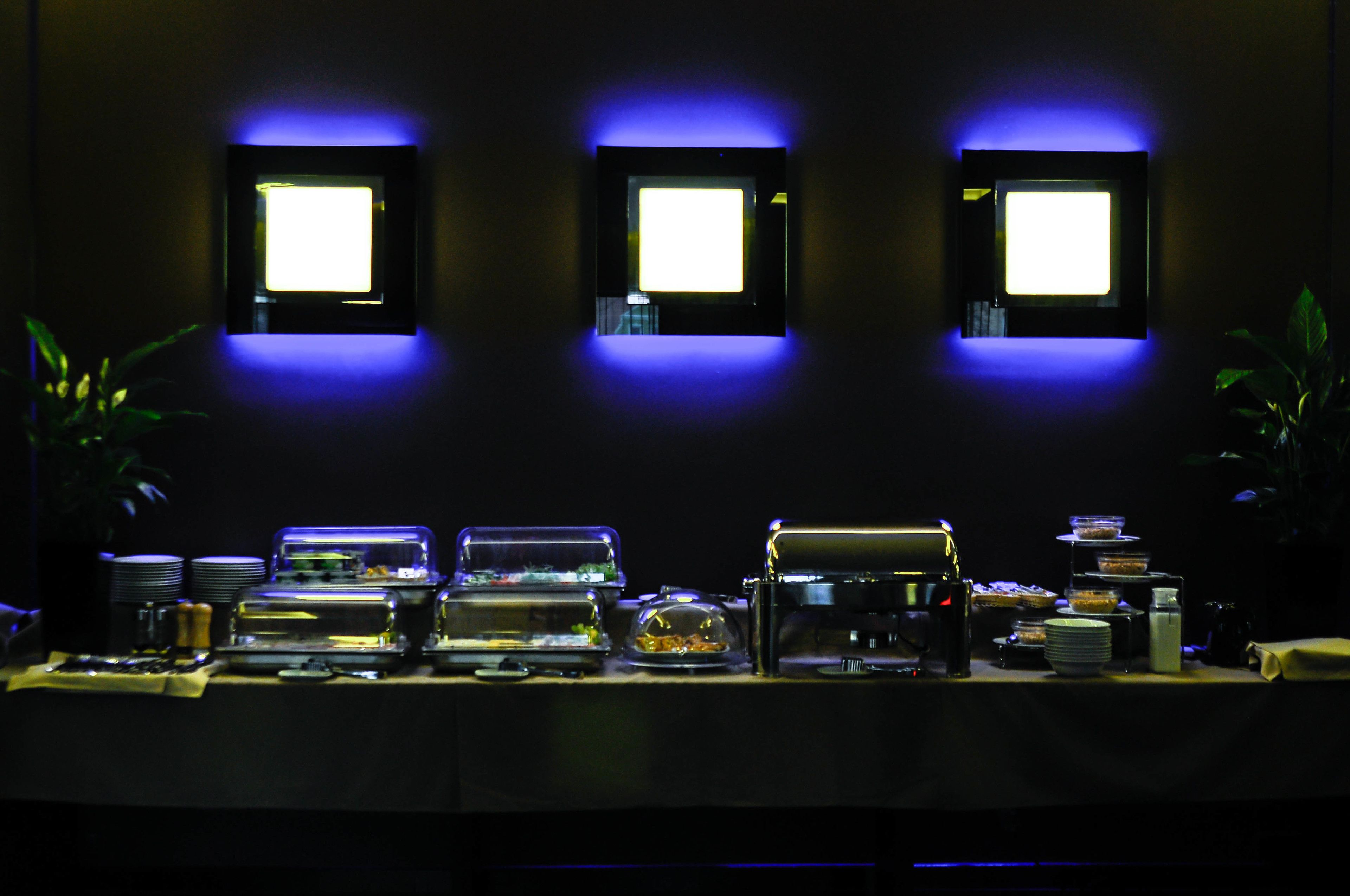Montaje tipo bufé con diversos alimentos y una máquina de café, iluminado con luces azules.