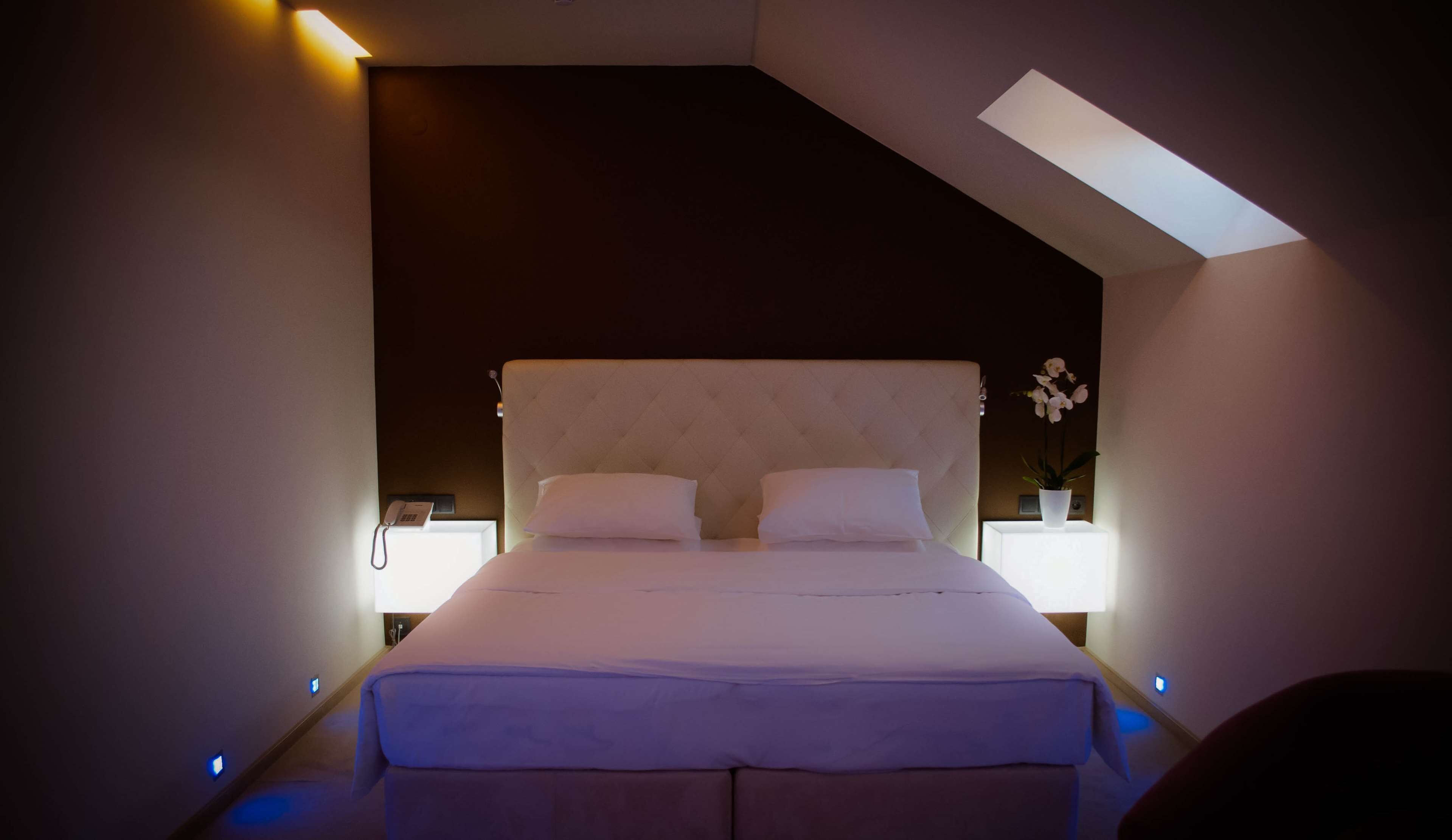 A modern bedroom with a large bed, two bedside tables with lamps, and a skylight.