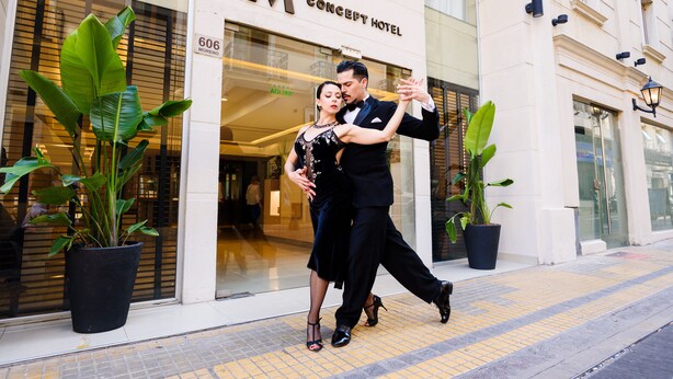A couple dancing in front of a hotel named 'Concept Hotel' with large potted plants and a clear entrance.