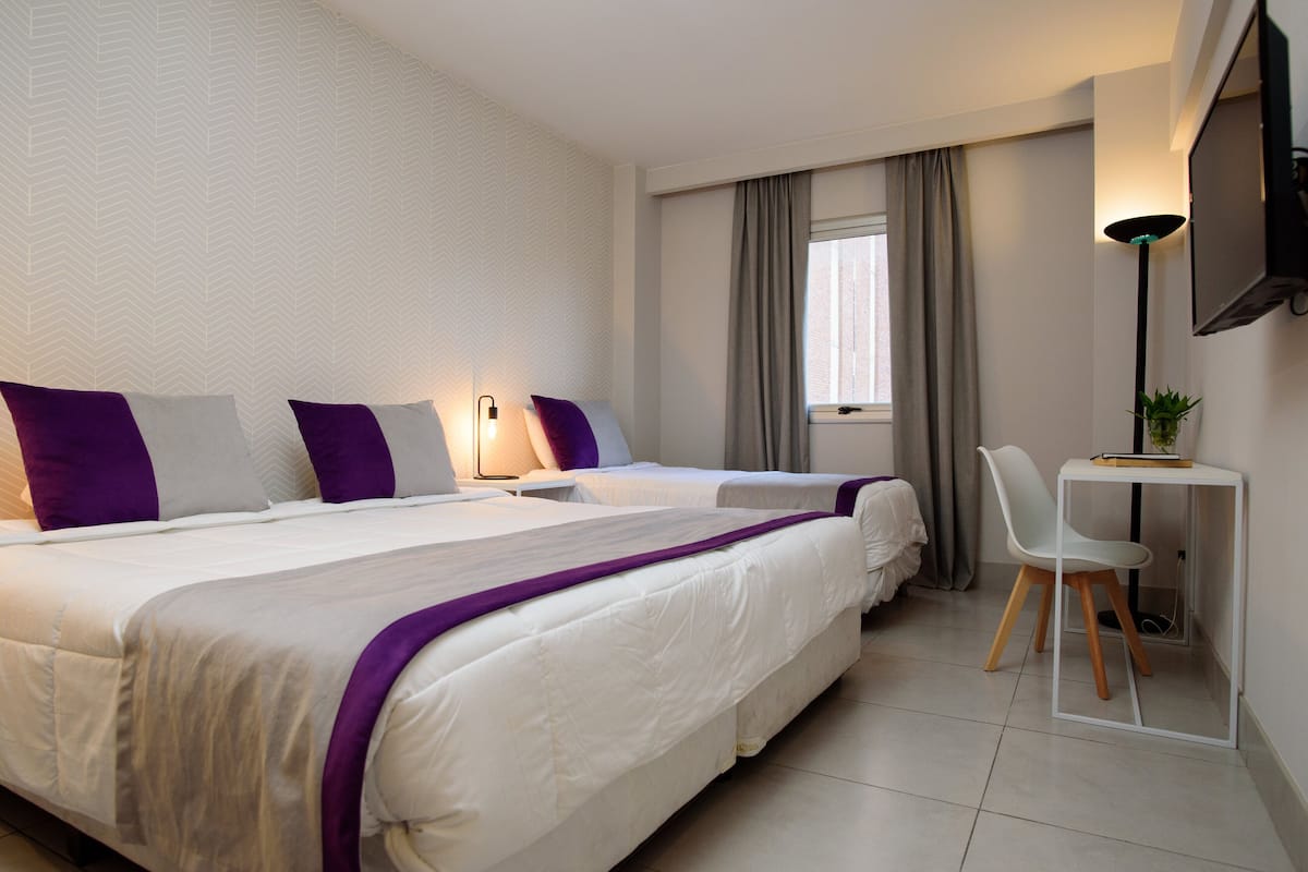 A hotel room with two beds, a desk, a chair, a TV, and a window with curtains.