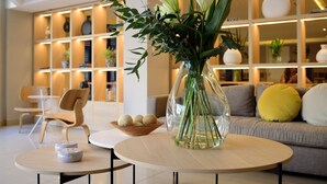 A modern living room with a round table, a vase with flowers, and a sofa with cushions.