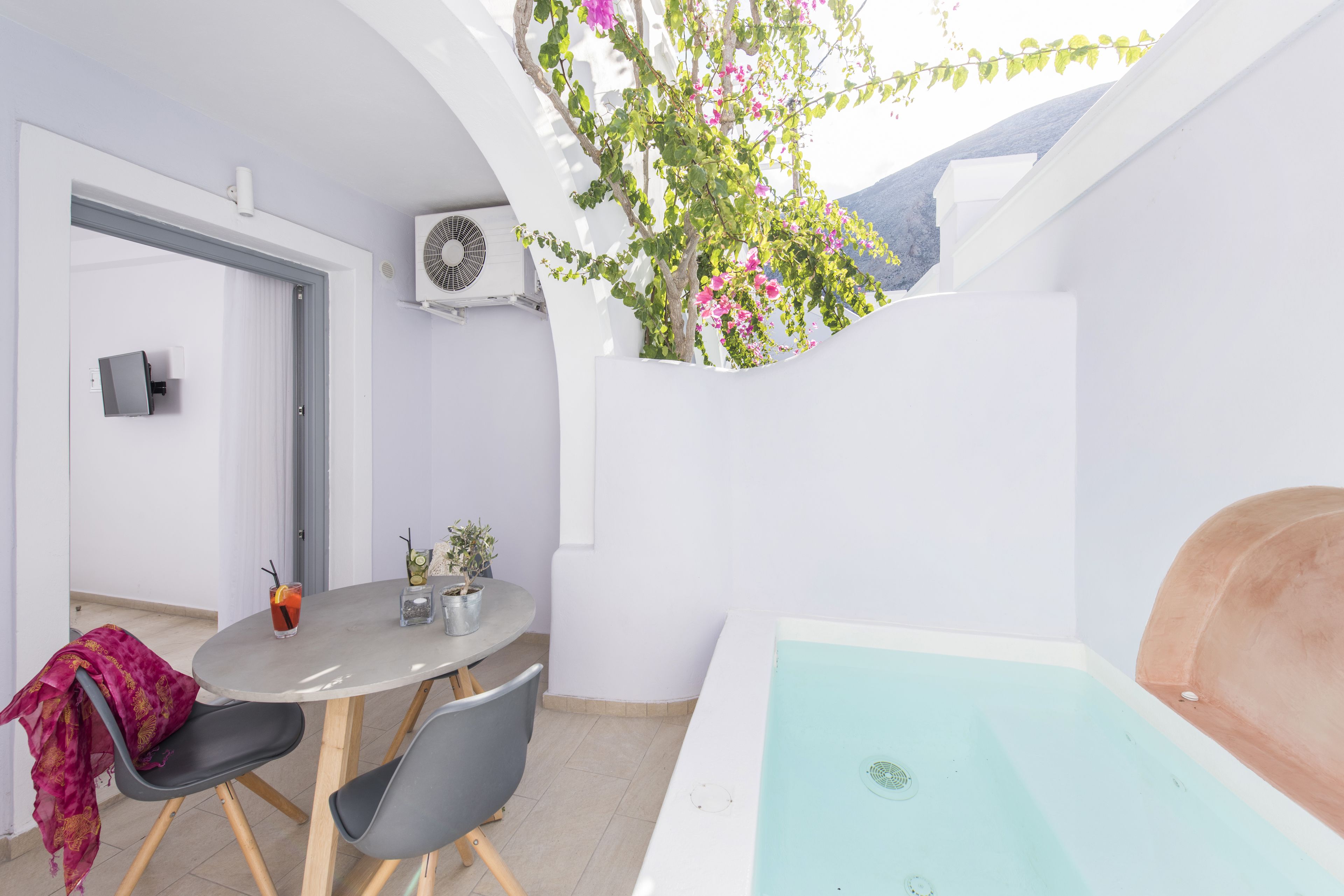 A modern room with a white ceiling, a round table with chairs, a small potted plant, a water feature, and a view of the outdoors.
