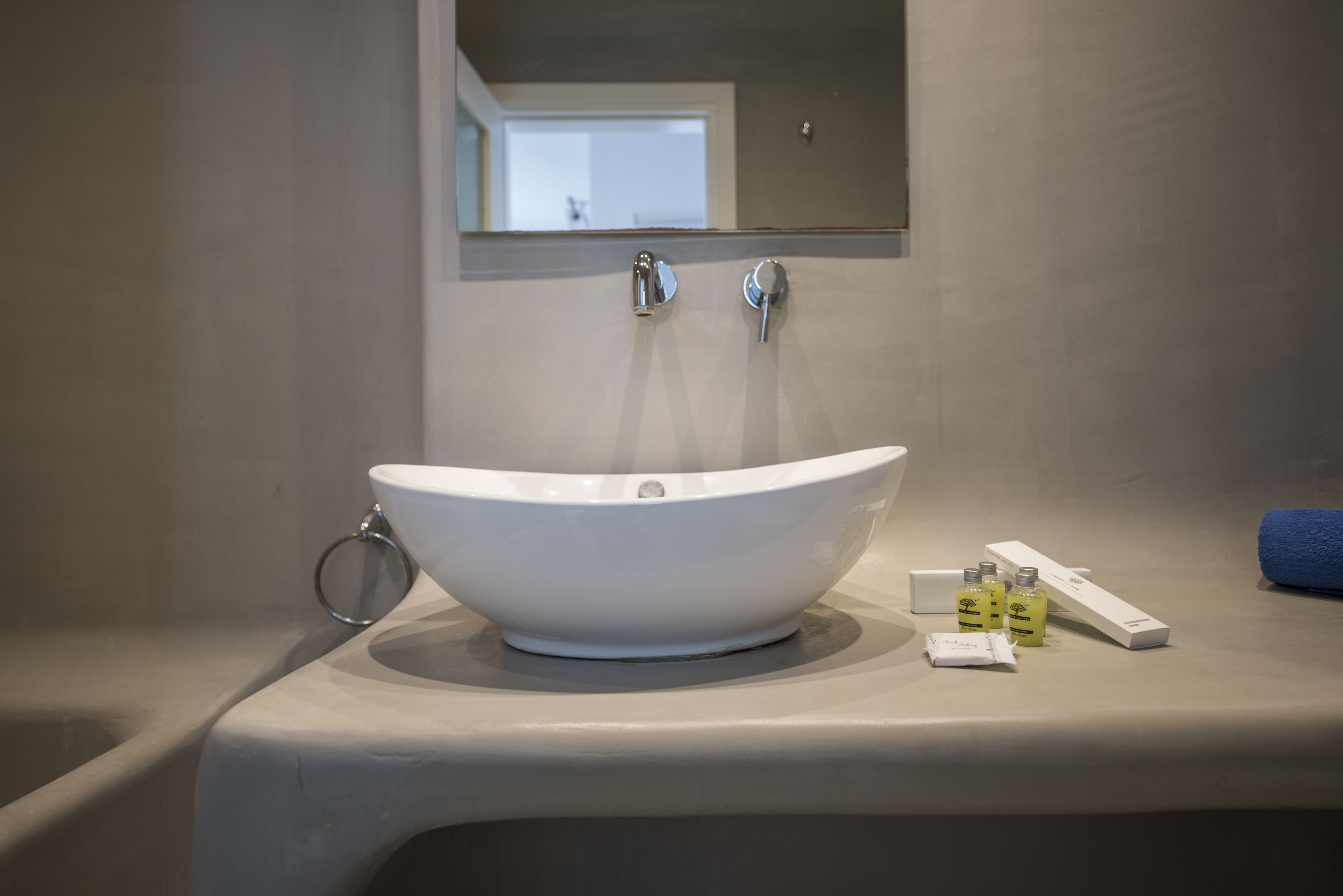 Un baño moderno con un lavamanos blanco, dos grifos y un espejo encima. Hay artículos de tocador en el borde del lavamanos.