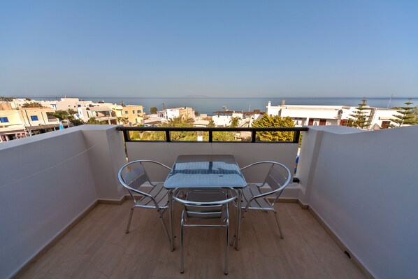 A balcony with a table and chairs, overlooking a cityscape and the sea. - Blue Waves Hotel (Santorini)