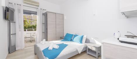 Una habitación de hotel moderna con una cama, una mesita de noche y un escritorio pequeño con una silla. Hay una ventana con cortinas, un televisor de pantalla plana montado en la pared y un ventilador de techo.