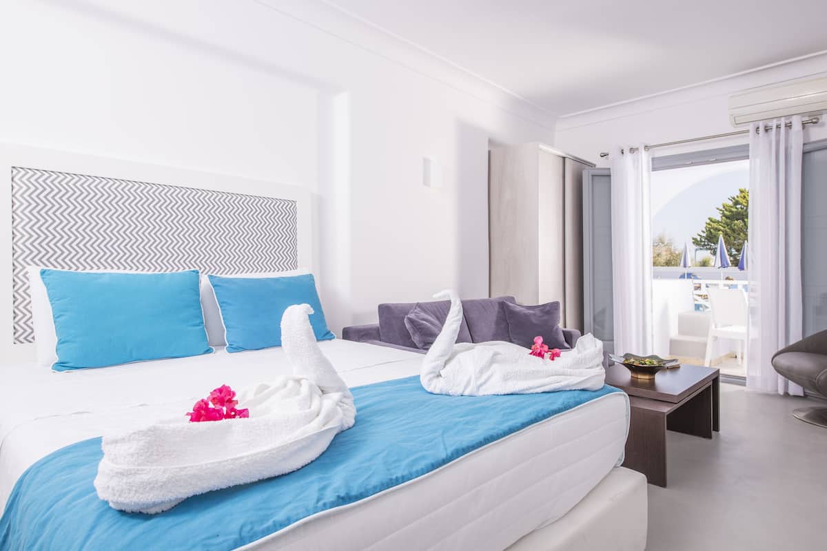 A hotel room with a bed, pillows, a blue blanket, a small table, and a chair.