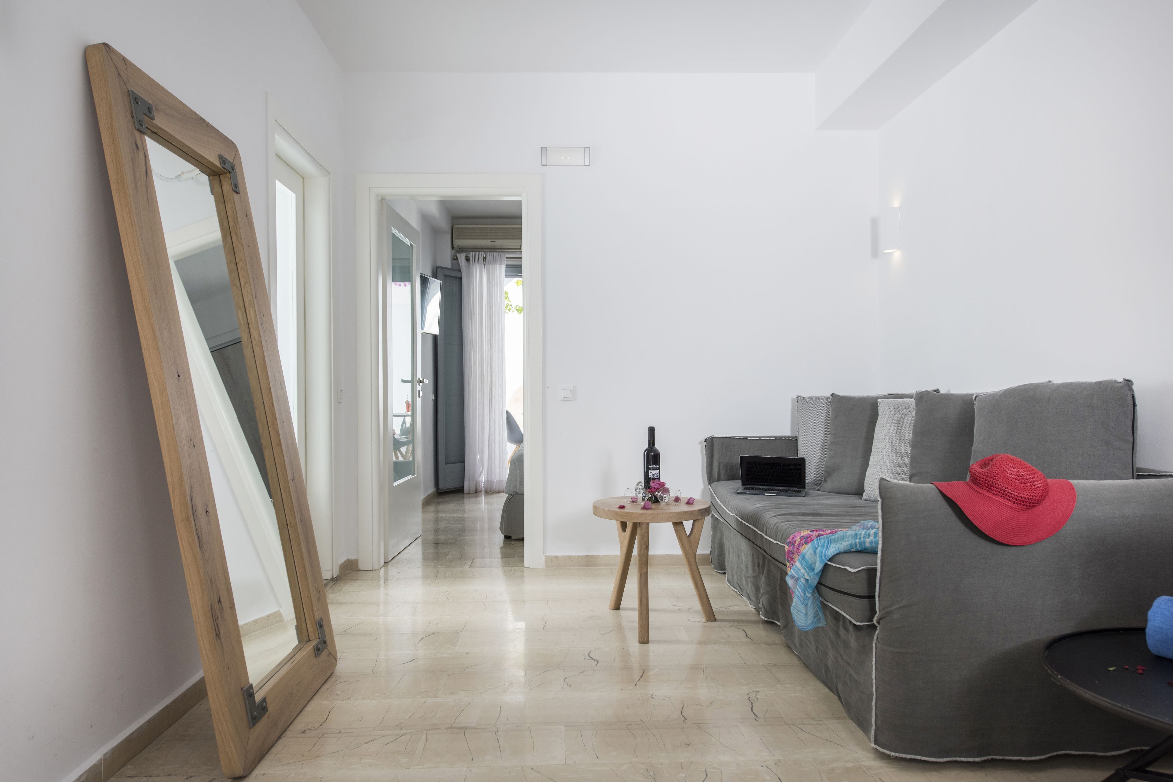 Ein modernes Wohnzimmer mit einem grauen Sofa, einem spiegel mit Holzrahmen und einem kleinen runden Tisch mit einer Flasche und Blumen.