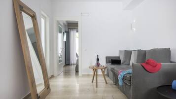 Ein modernes Wohnzimmer mit einem grauen Sofa, einem spiegel mit Holzrahmen und einem kleinen runden Tisch mit einer Flasche und Blumen.