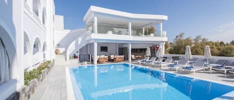 A modern pool area with a clear blue pool, lounge chairs, and a two-story building with balconies.