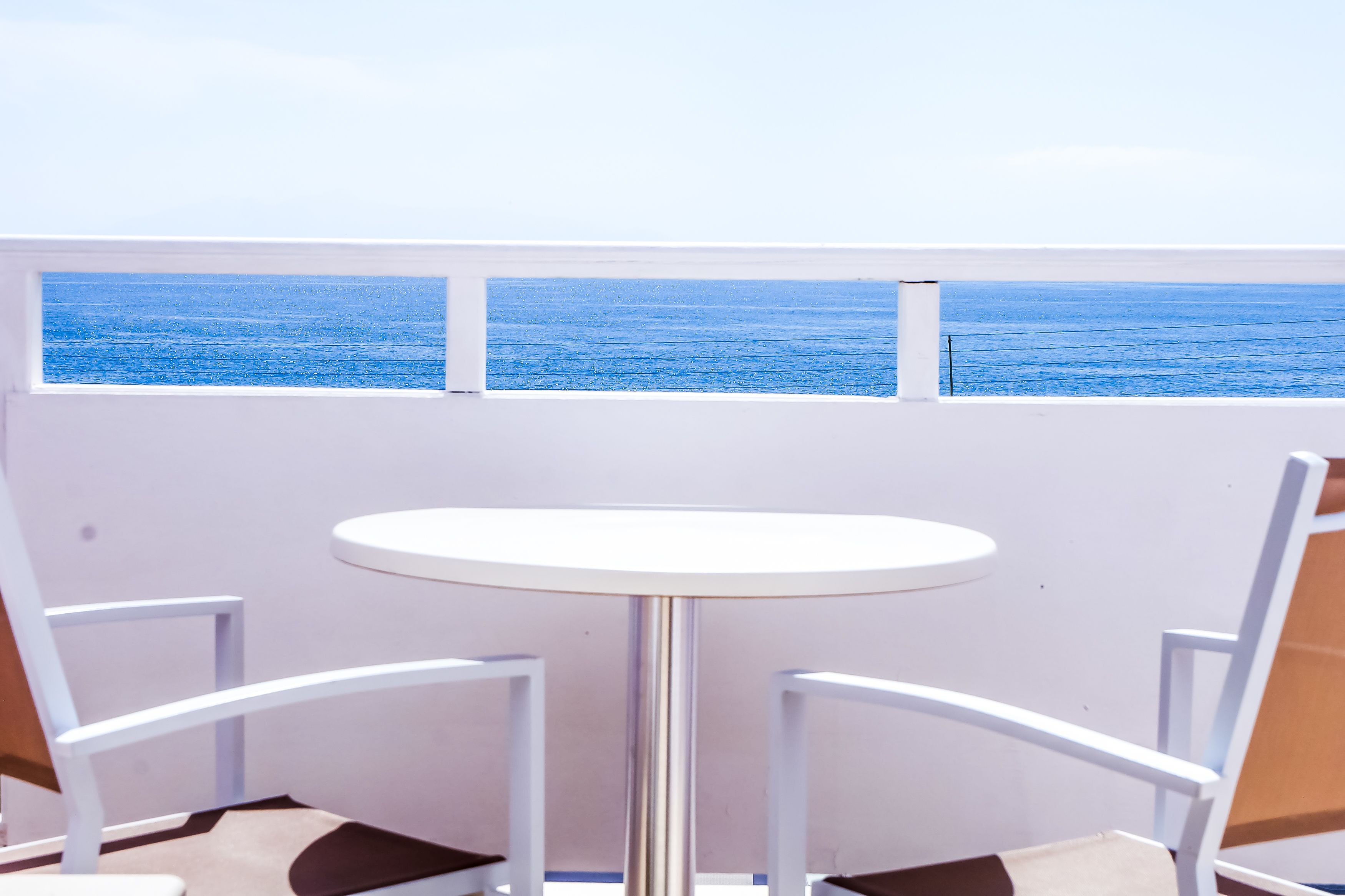 A white table and chairs with a view of the ocean through a window.