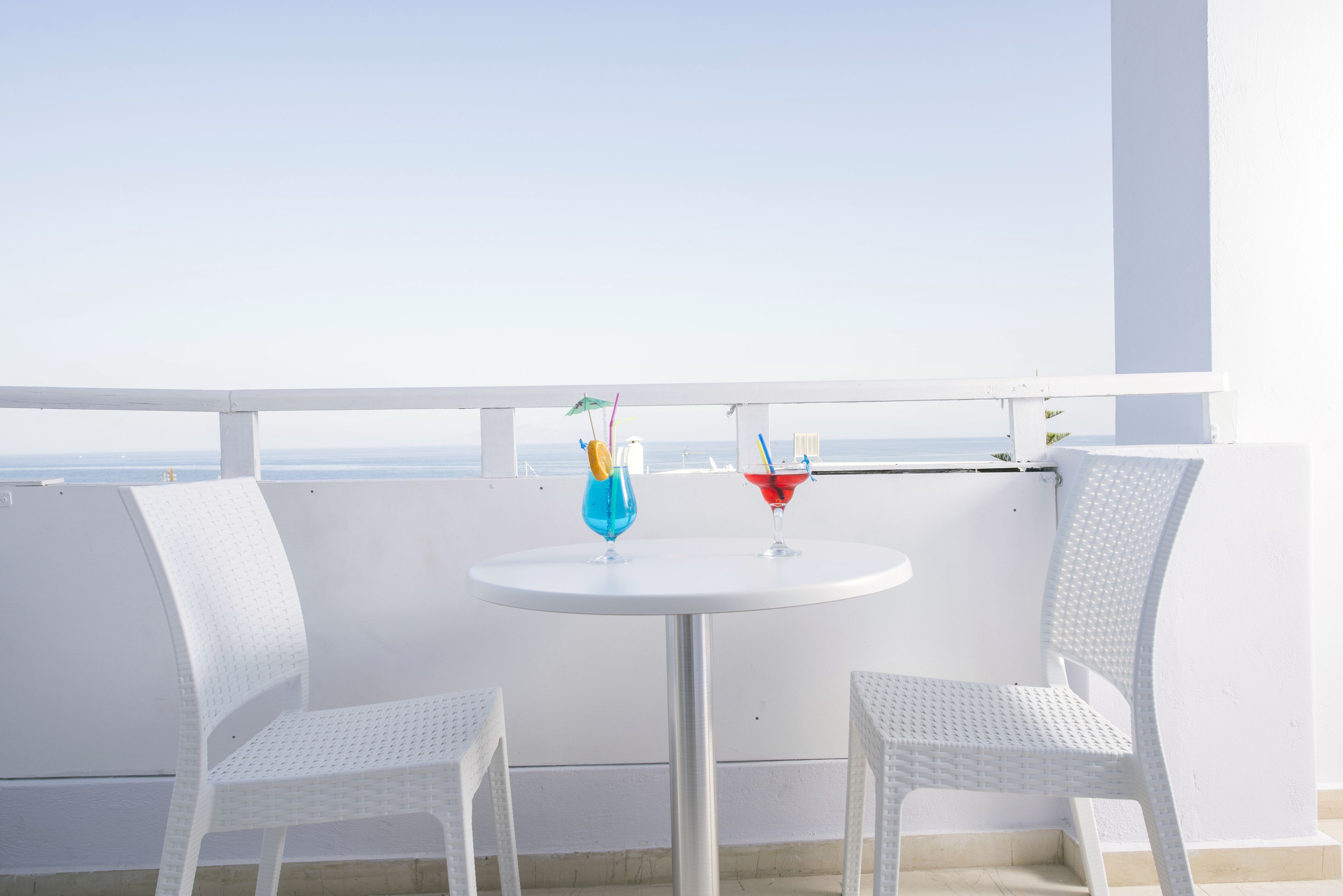 A white outdoor seating area with two chairs and a round table, featuring two colorful drinks.