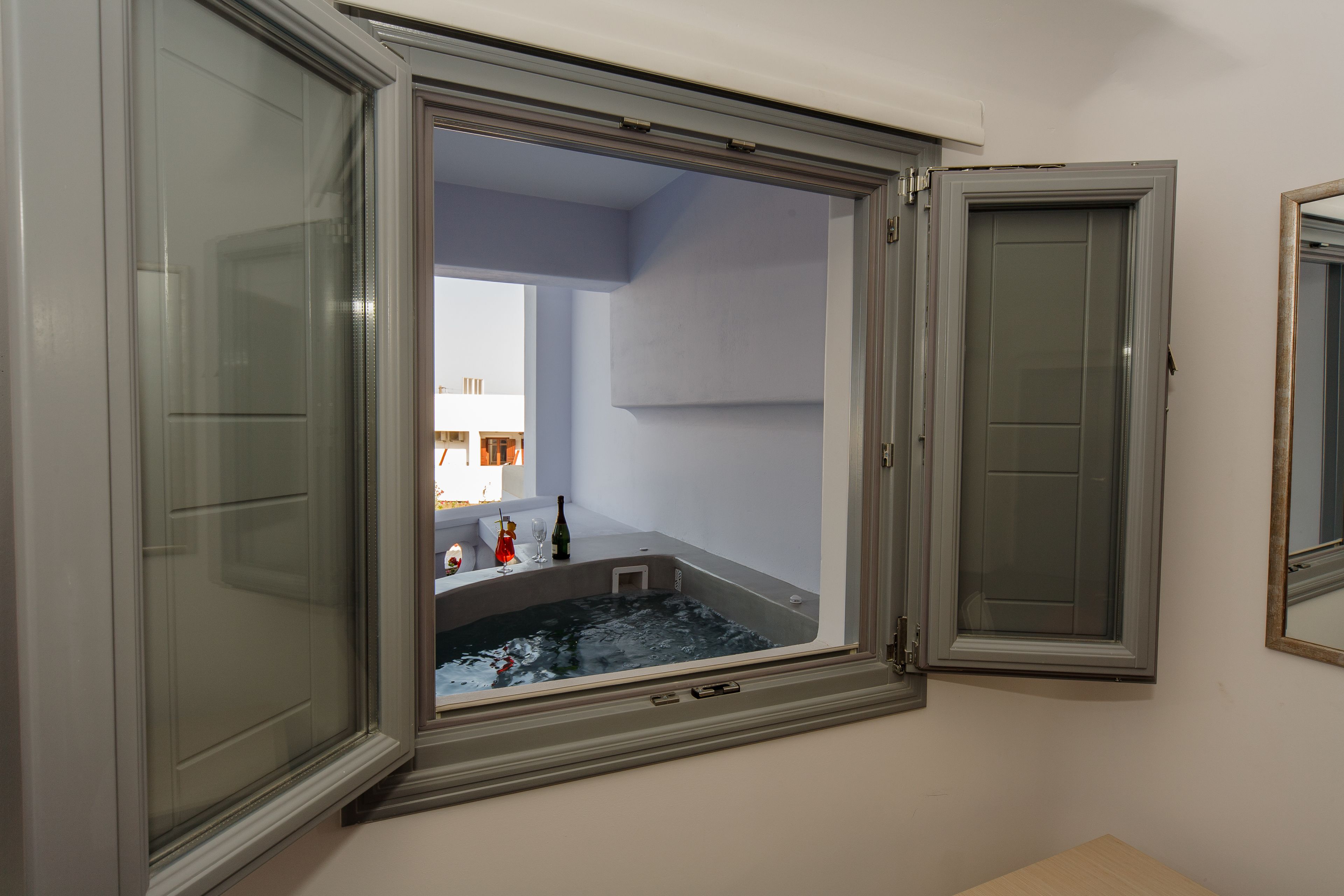 A room with a large window, a bathtub, and a mirror.