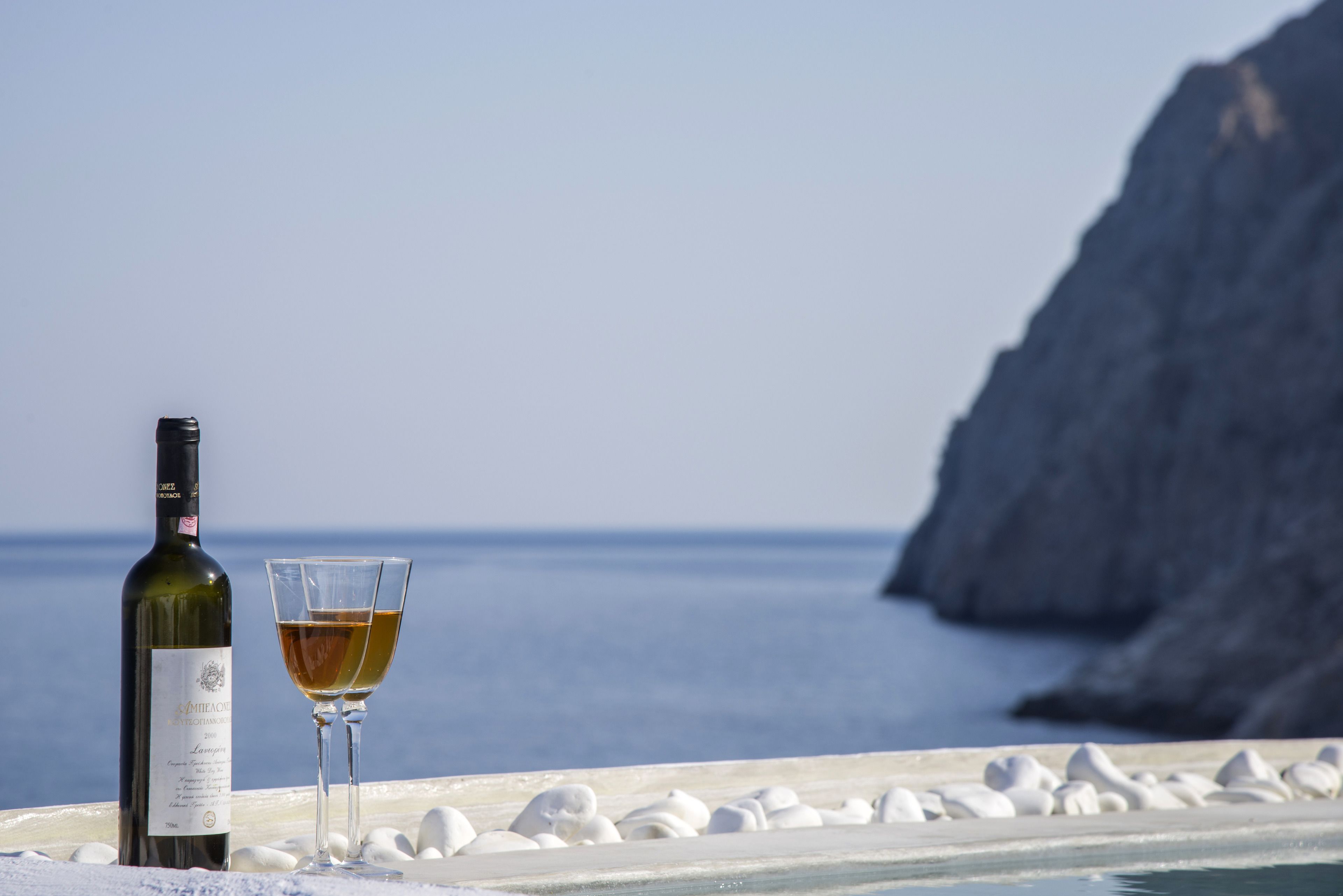 Eine Weinflasche und ein Glas auf einem Balkon mit Blick auf das Meer und eine Felsklippe.
