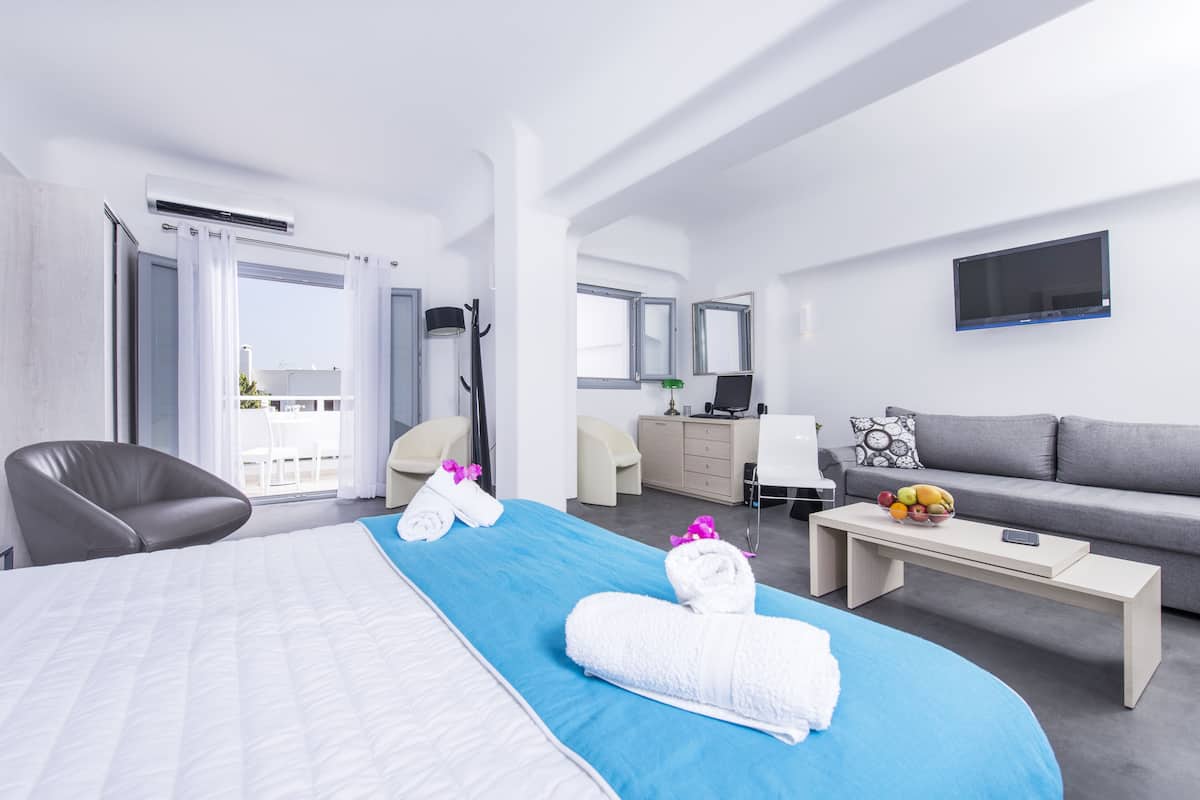 A modern hotel room with a large bed, a sofa, a desk, and a TV.