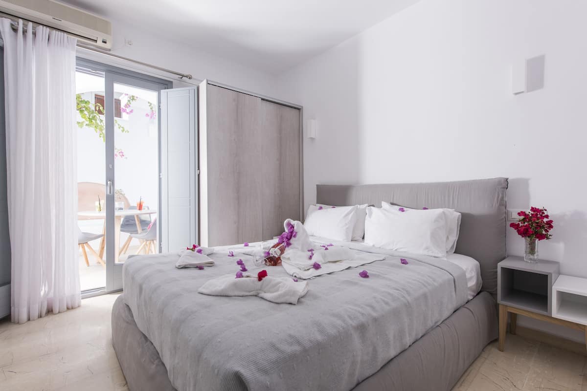 A hotel room with a bed, a nightstand, a small table, and a sliding door leading to an outdoor area.
