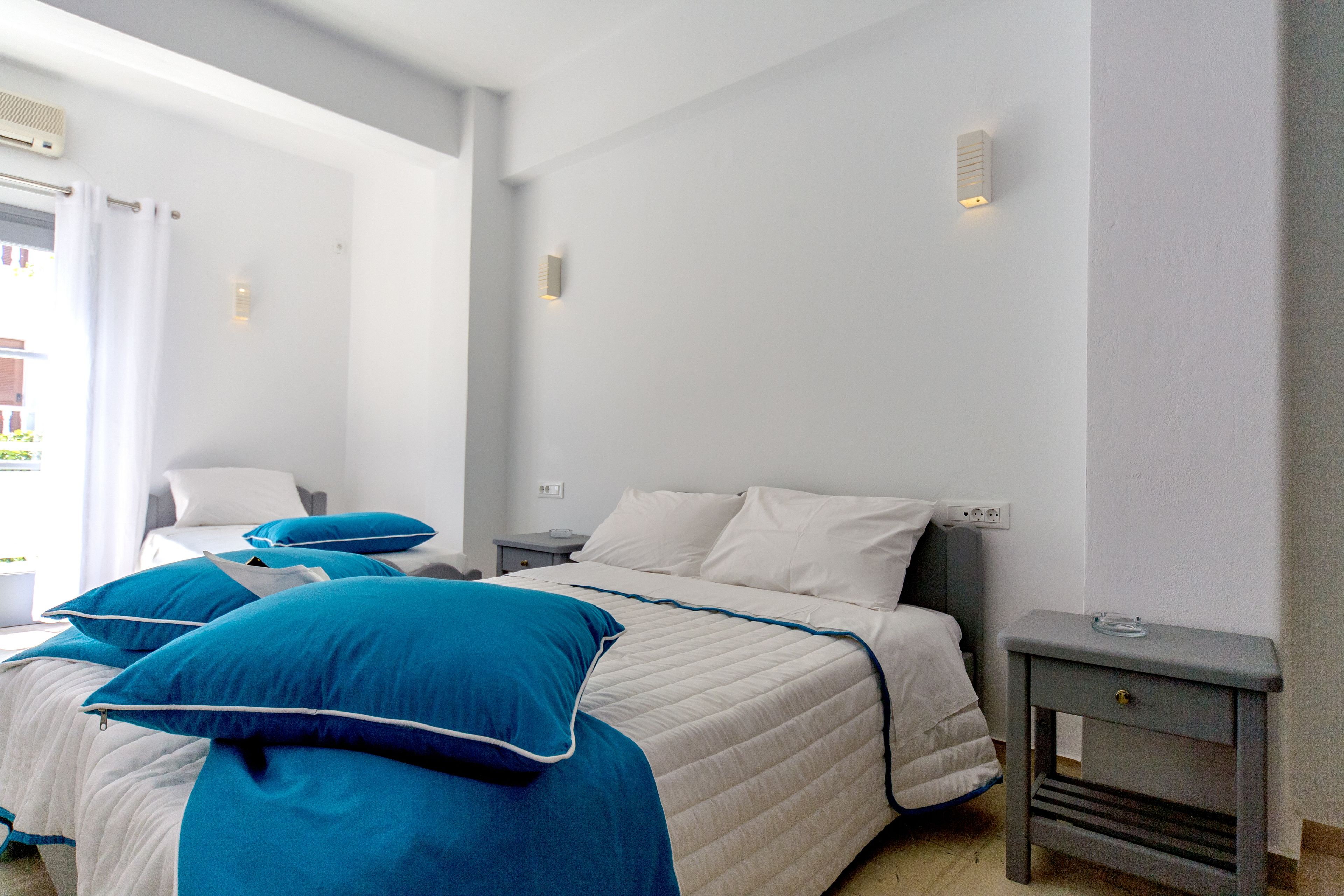 Un dormitorio con cama, mesitas de noche y una ventana con cortinas.