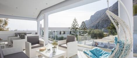 Un espace extérieur moderne, aménagé avec des meubles en osier blanc, un fauteuil suspendu et une table en verre.