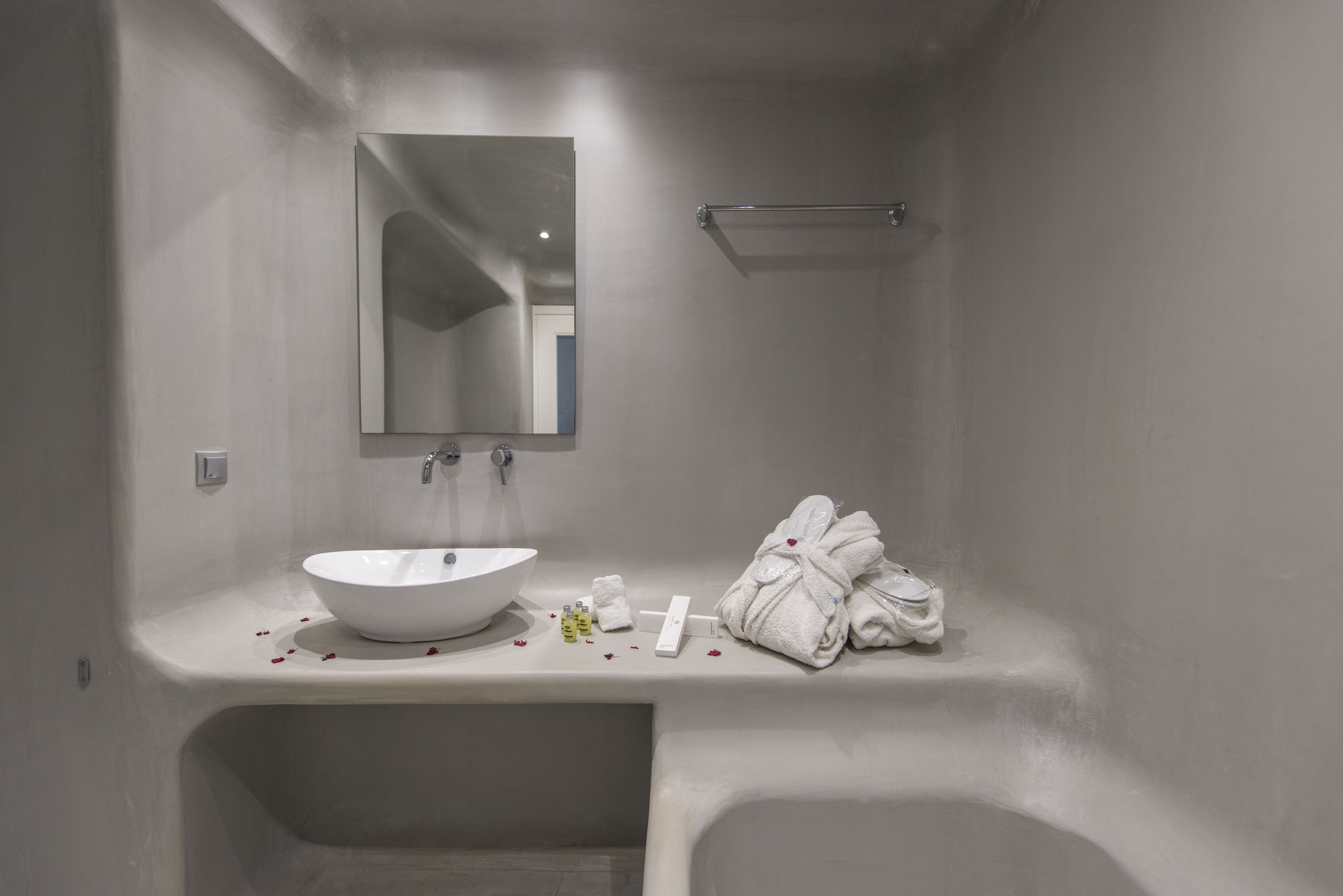 Ein modernes Badezimmer mit einem weißen Waschbecken, Spiegel und einer Badewanne. Auf der Ablage liegen Handtücher und Pflegeartikel.