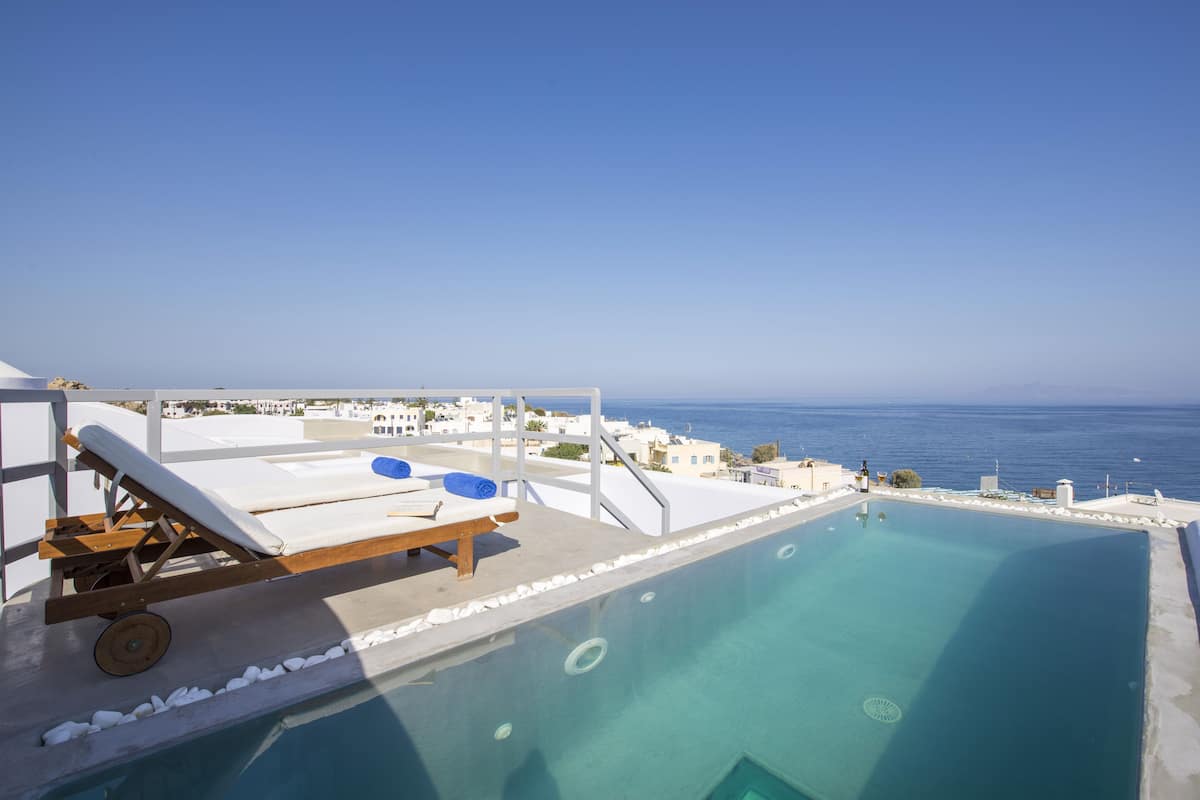 A rooftop infinity pool with a lounge chair and a towel, overlooking a coastal cityscape.