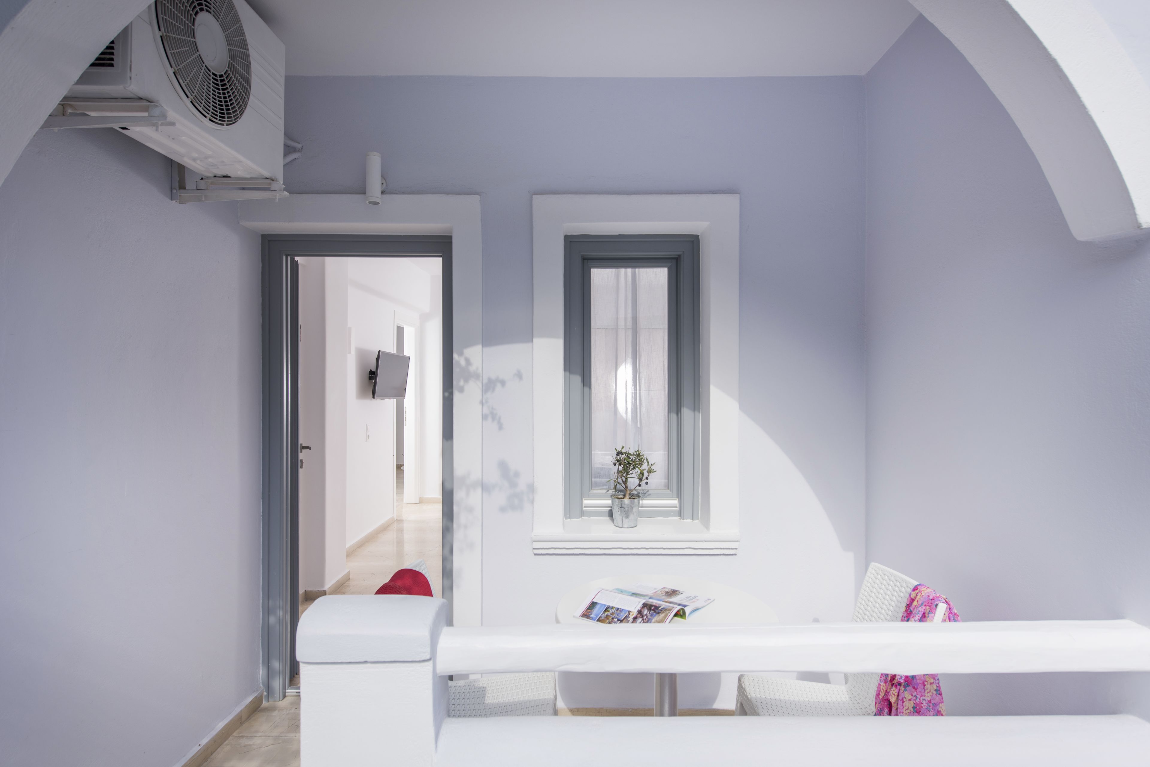 Una habitación moderna y minimalista con un banco blanco, una mesita con una revista y una ventana con una planta.