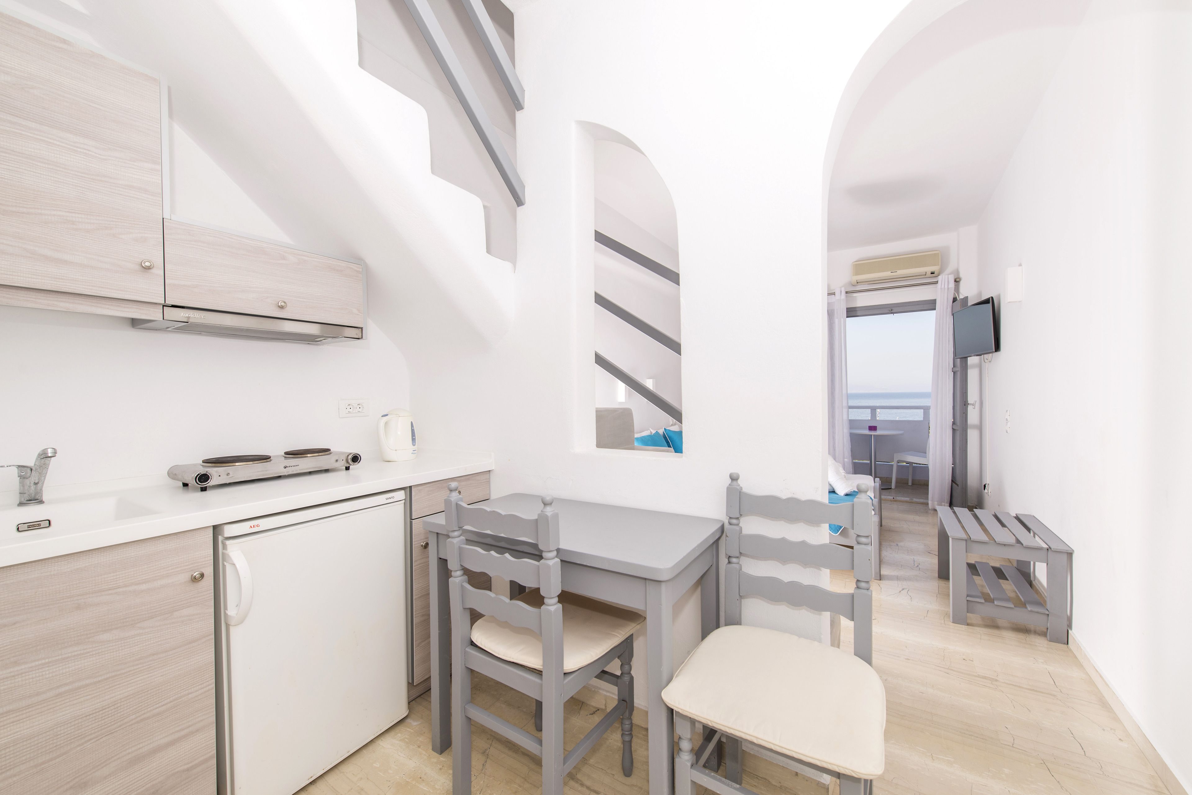 Une cuisine compacte dotée d’un réfrigérateur intégré, d’une petite table à manger avec deux chaises et d’une vue sur l’extérieur grâce à une fenêtre en arc de cercle.