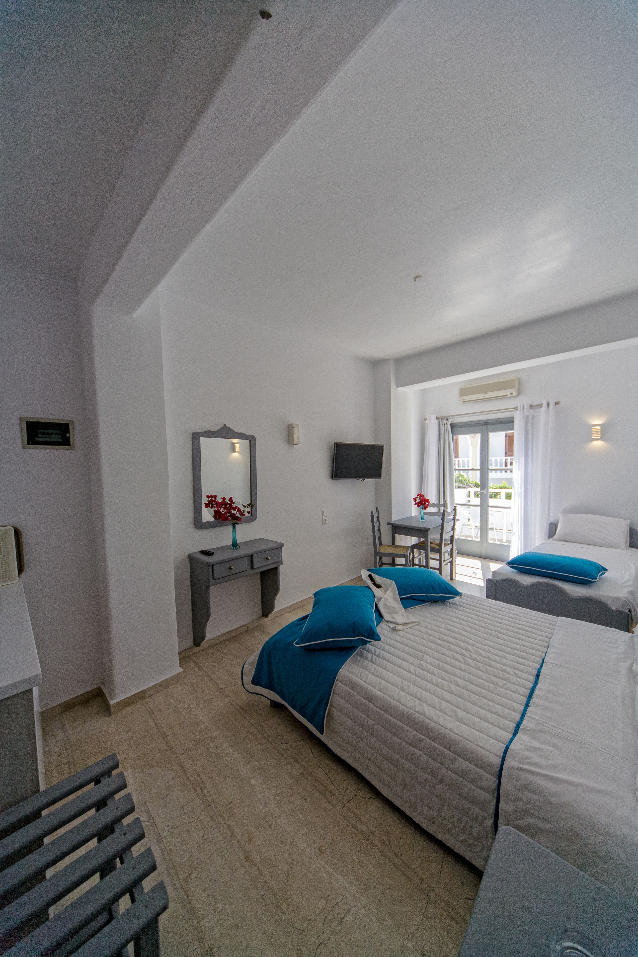 Une chambre d’hôtel avec deux lits, un bureau, une chaise, une télévision et un balcon équipé d’une table et de chaises.