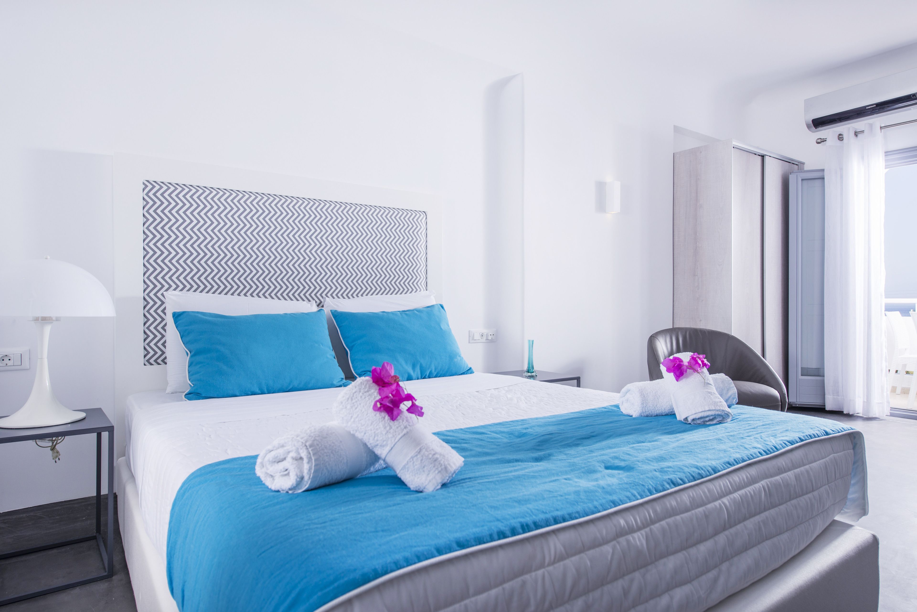 Una camera d'albergo con un letto grande, due cuscini, un comodino con una lampada e una sedia.