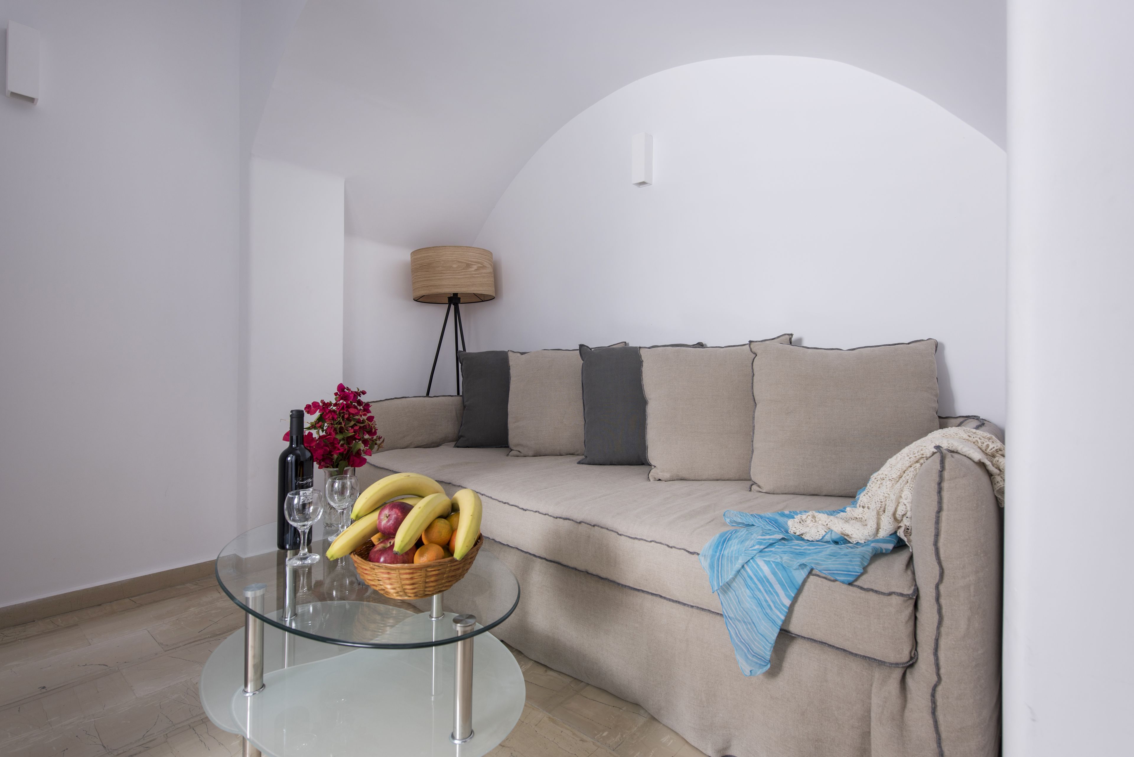 Una sala de estar con una mesa de centro de vidrio, un sofá color beige y una lámpara.
