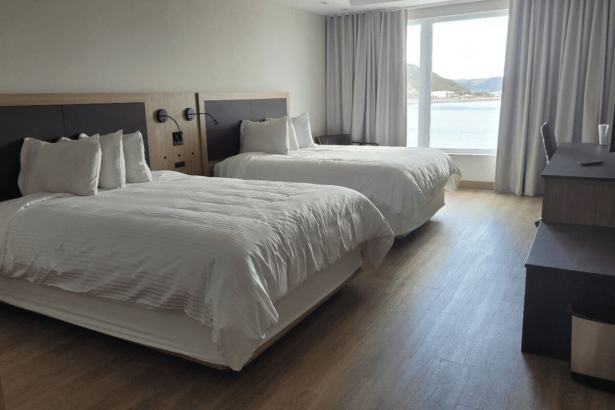 Een hotelkamer met twee bedden, een bureau en uitzicht op zee.