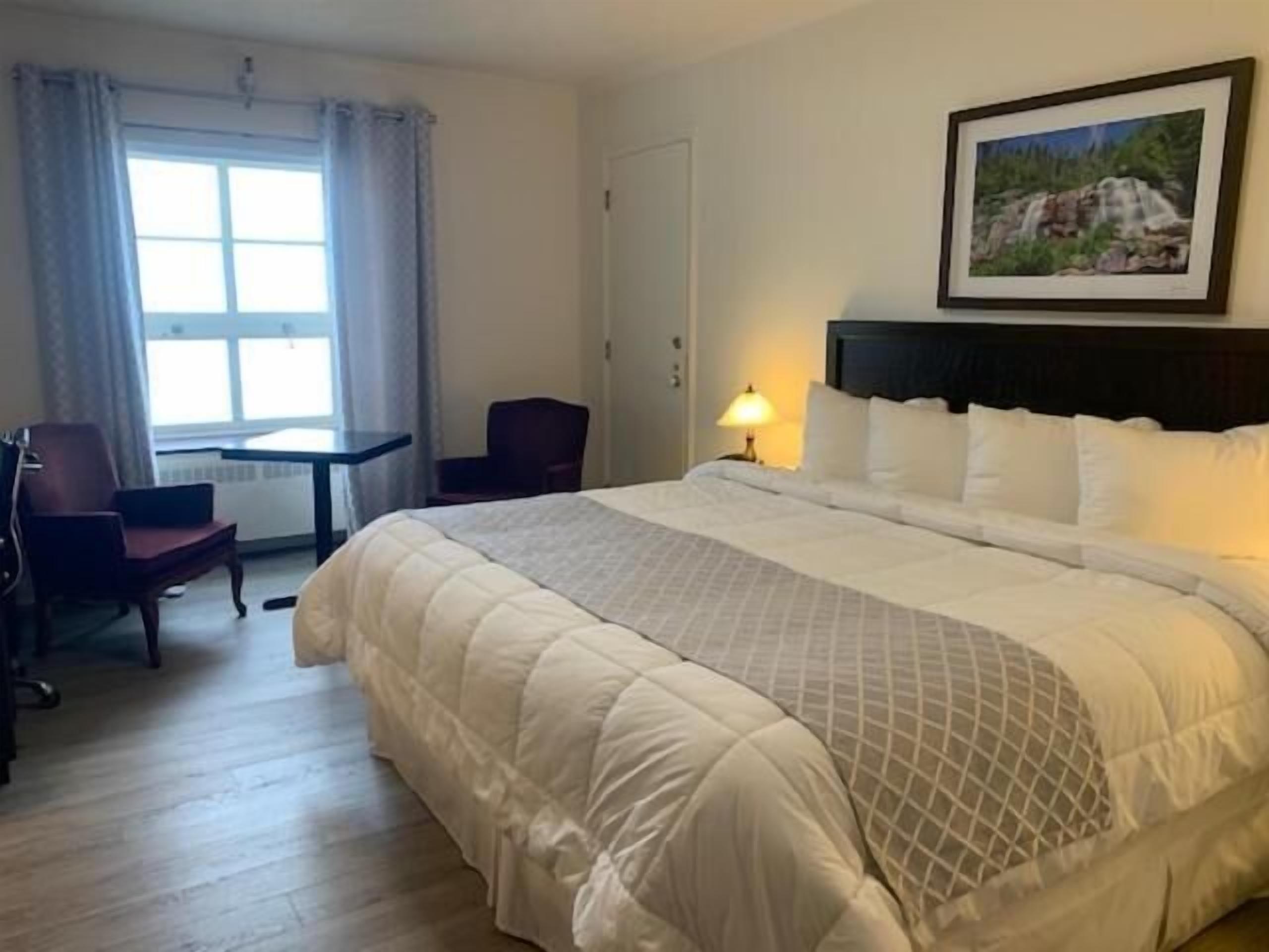 Habitación de hotel con una cama grande, un escritorio, una silla y un cuadro en la pared.