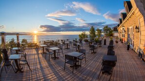 Terraza de madera con mesas y sillas, con vista a un cuerpo de agua durante el atardecer.