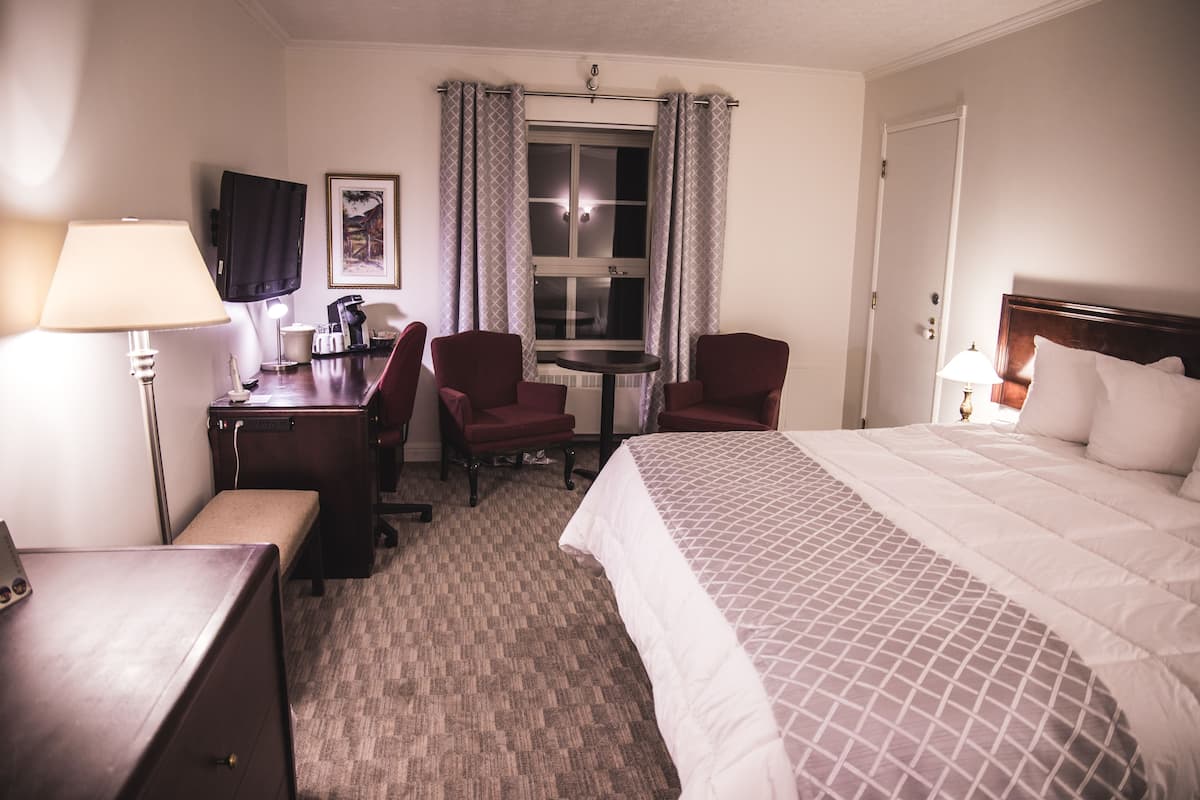 Een hotelkamer met een bed, bureau, stoelen, een klein tafeltje en een raam met gordijnen.