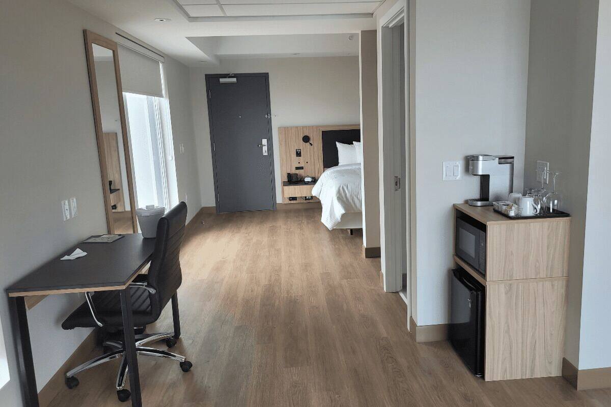 Een hotelkamer met een houten vloer, een bureau met stoel, een bed, een kledingkast, een magnetron en een koffiezetapparaat.