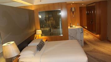 A hotel room with a large bed, a bedside table with a lamp, a telephone, and a mirror. There is a small bathroom with a sink and a mirror.